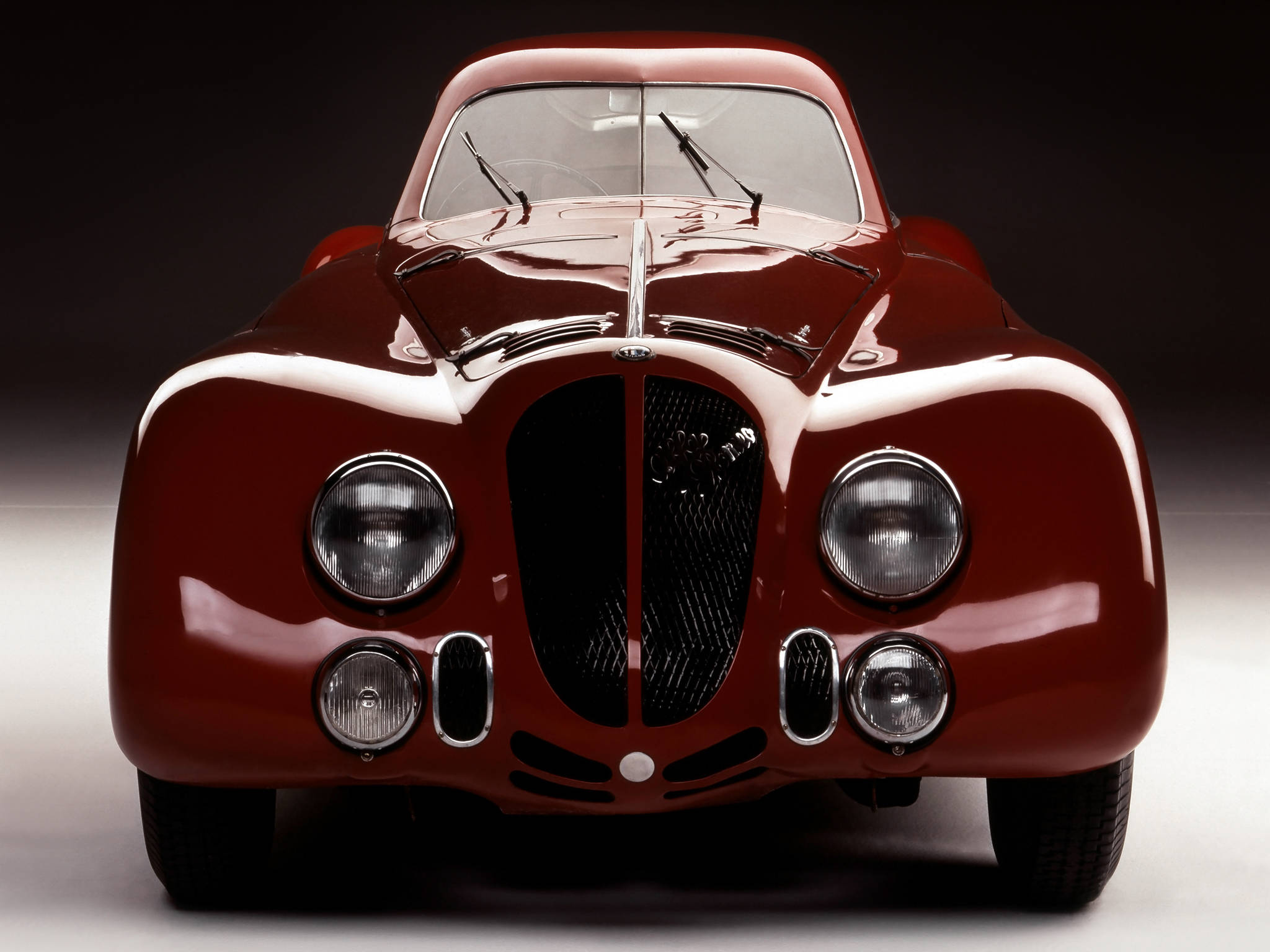 暗室中經典復古紅色Alfa Romeo iPhone壁紙 壁紙 — 一輛光澤的紅色復古跑車，帶有鍍鉻裝飾和圓形頭燈，在攝影棚內以深色漸變背景拍攝。