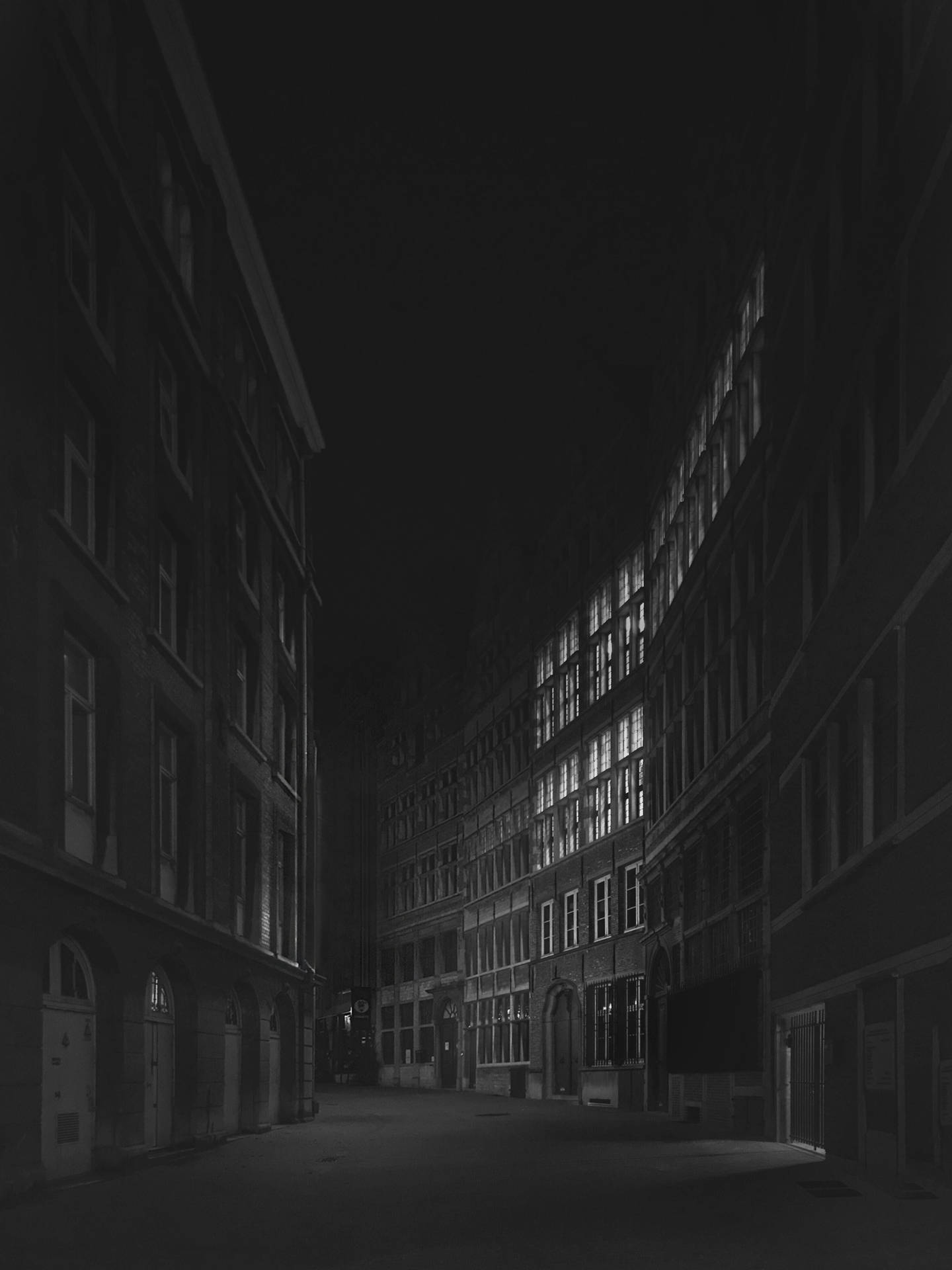 夜晚黑暗的城市小巷，高樓大廈中有明亮的窗戶。