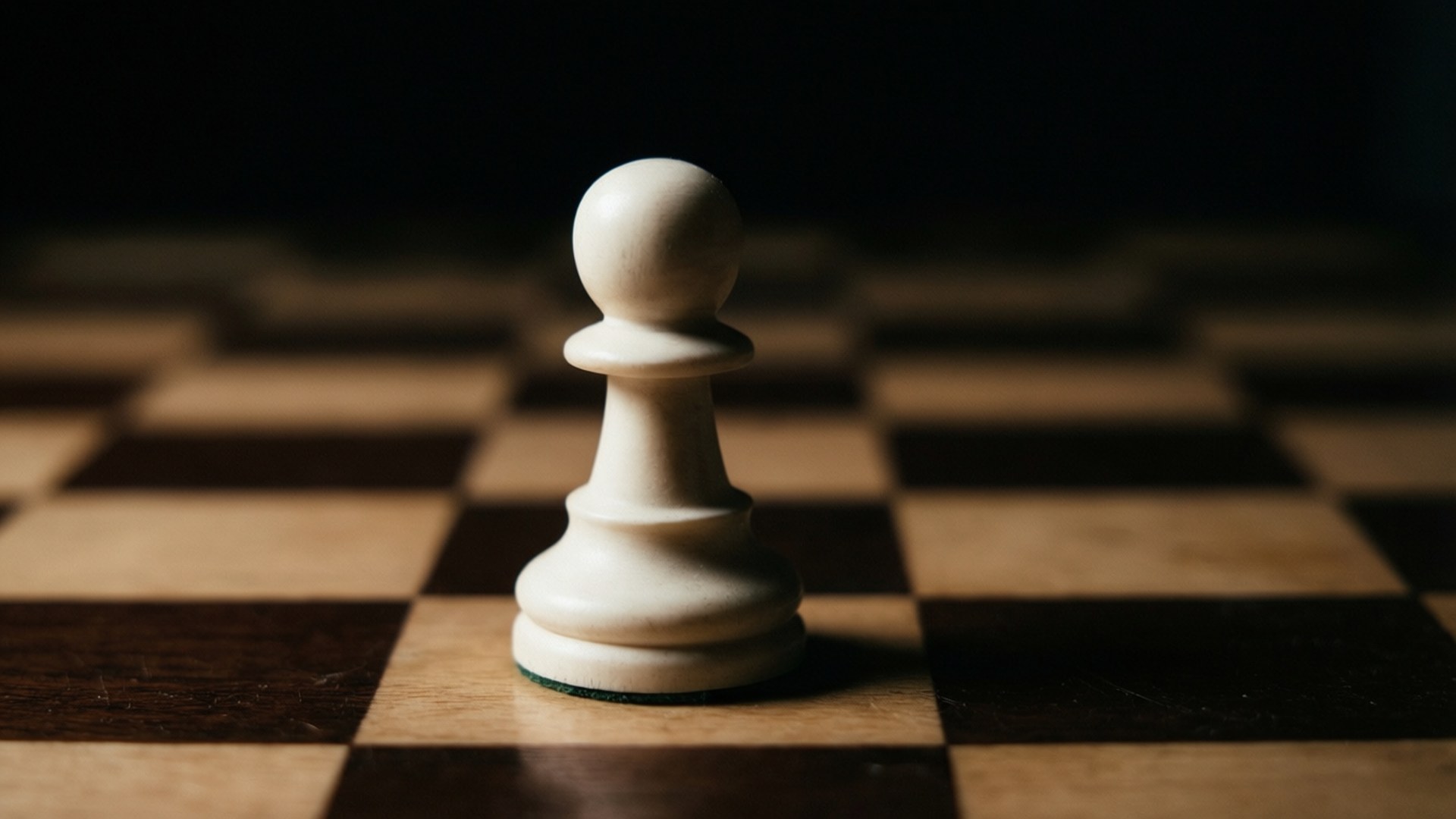 暗影中的孤單兵卒 壁紙 — 一個白色國際象棋兵卒在木製棋盤上清晰對焦，模糊的方格逐漸消失在黑暗中。