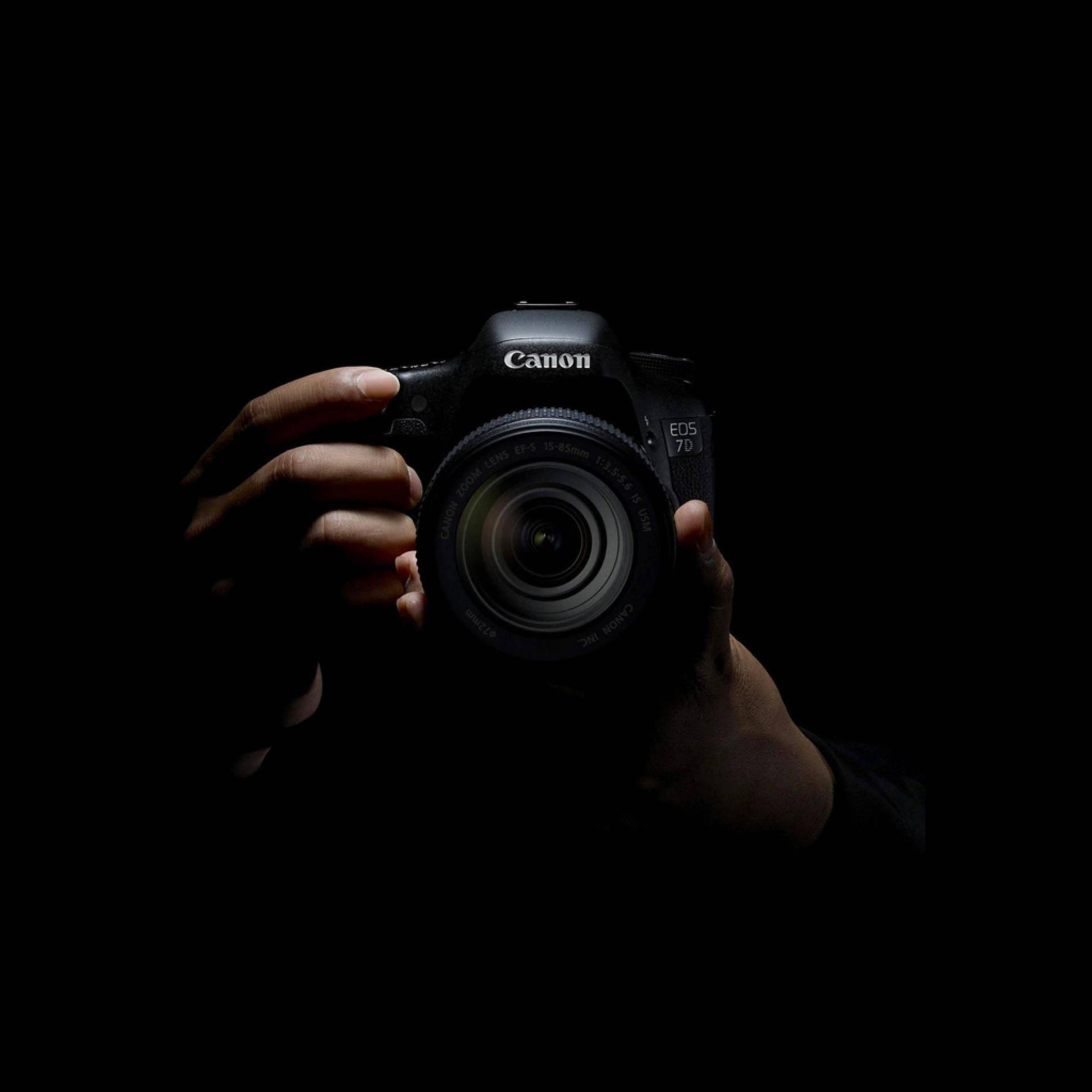 在黑暗的攝影棚燈光下拿著Canon EOS 7D相機的手。