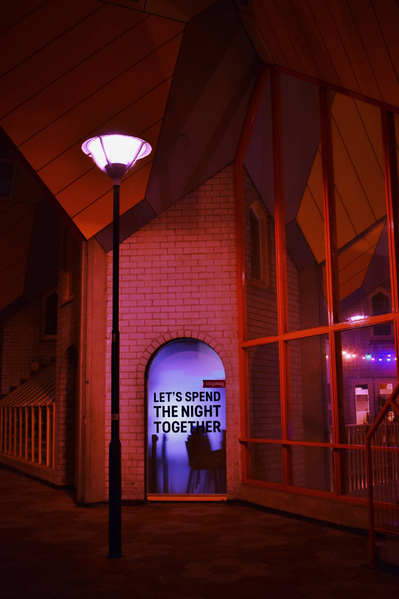 盞發光嘅街燈照亮咗一棟現代建築嘅入口，上面有句『LET'S SPEND THE NIGHT TOGETHER』。