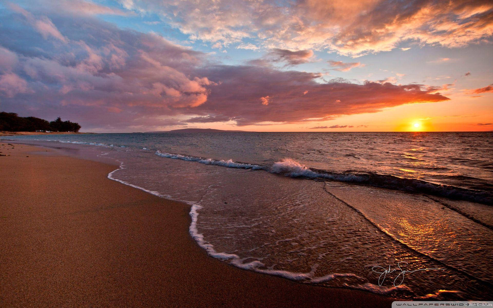 暗色沙灘上的日落美景 壁紙 — 夕陽將天空染成火熱的橙色和粉紅色，海浪輕輕拍打著沙灘。