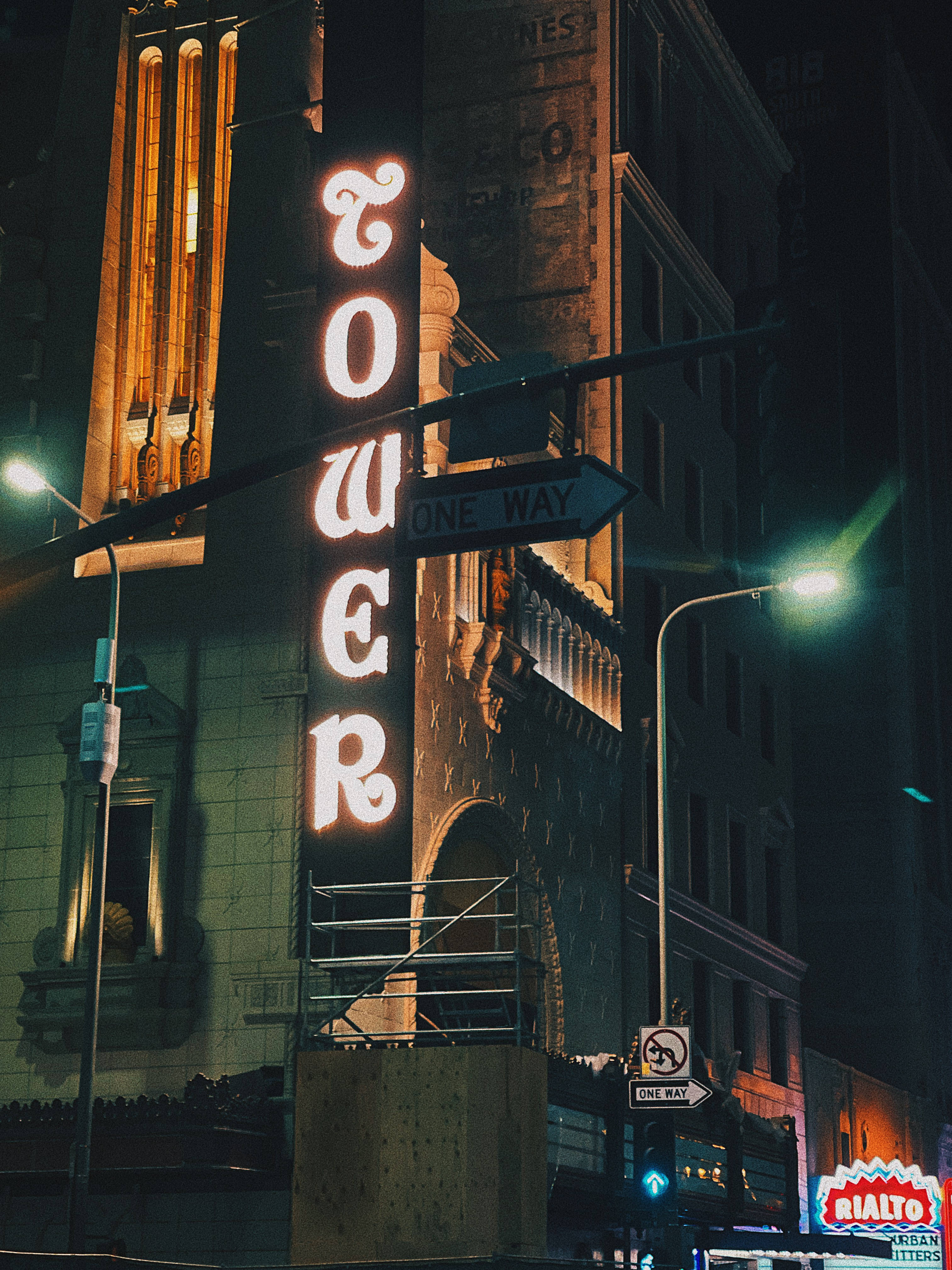 暗色霓虹 iPhone 高樓建築 壁紙 — 一個發光的霓虹燈牌，上面寫著「TOWER」，照亮了夜晚骯髒的城市小巷，伴隨著街燈和復古建築。