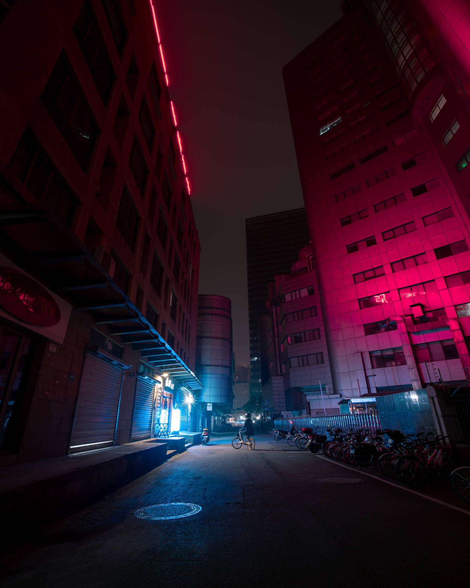 夜間城市小巷，帶有霓虹燈和一名騎單車者。