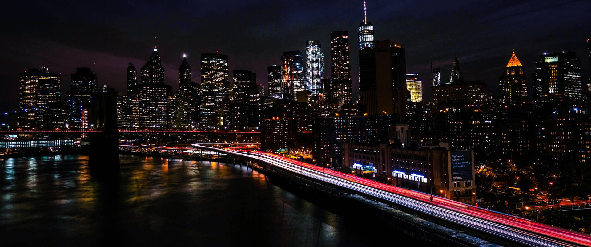紐約天際線的夜景，橋樑上燈火通明的建築物和交通燈光軌跡。