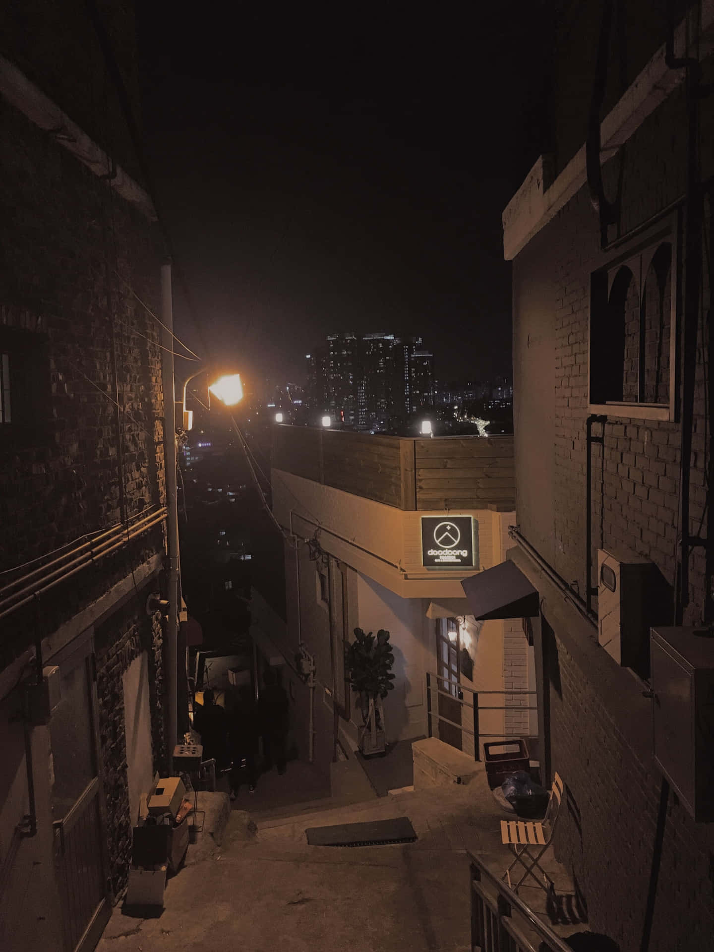 夜晚狹窄的磚砌小巷，溫暖的街燈和遠處的城市天際線。