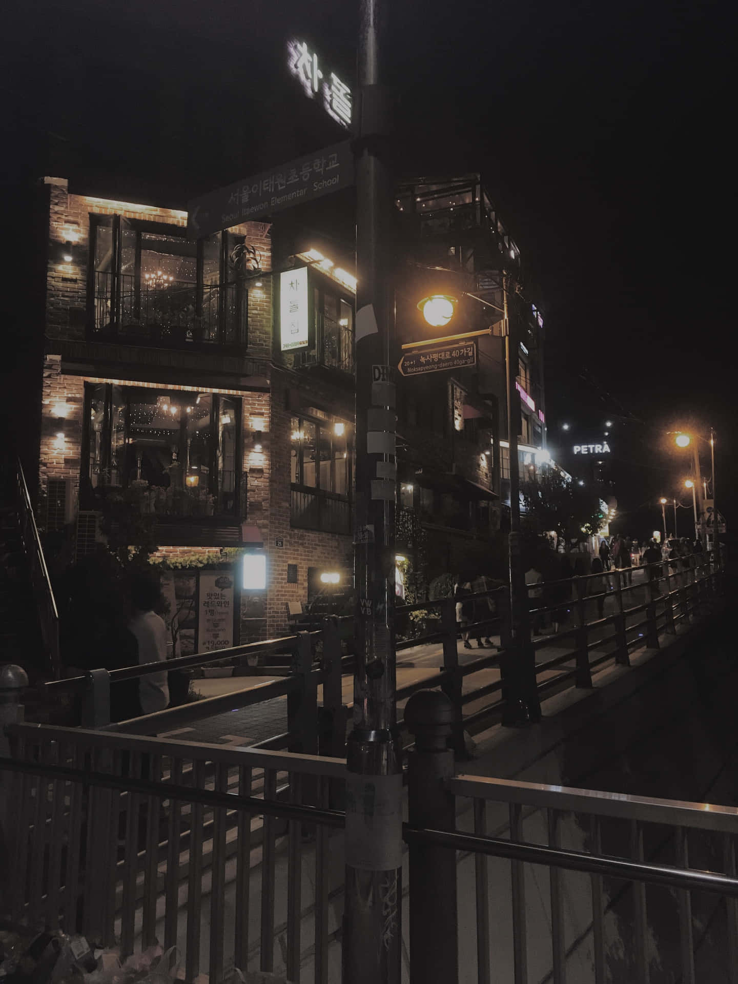 夜晚的城市街道，有發光的招牌和沿著欄杆行走的行人。