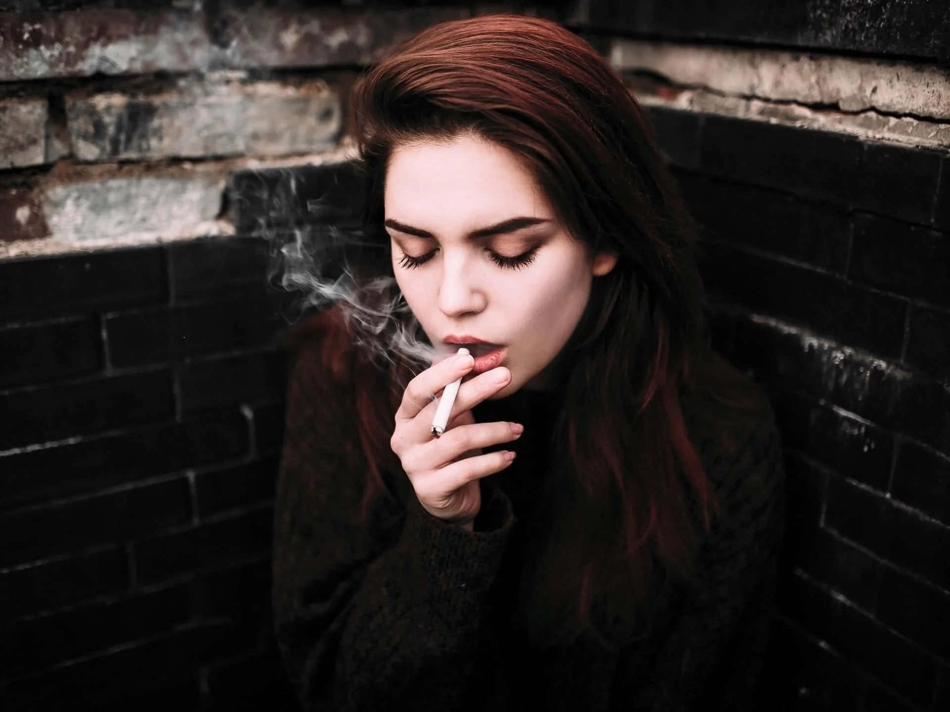 紅髮女子在深色磚牆旁吸煙。
