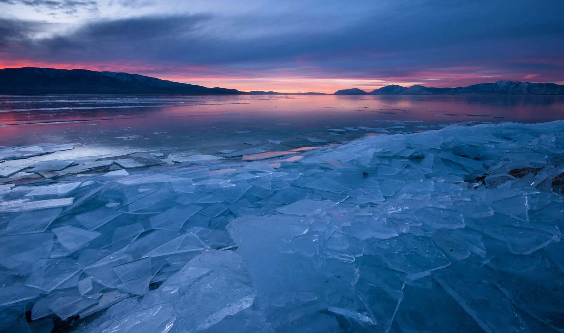 Frozen Lake 桌布 壁紙 — 暮色中的冰凍湖面，破碎的冰塊反射著遠處雪山上的粉紫色天空。