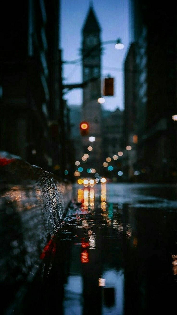 黃昏時分下雨的城市街道，發光的路燈和遠處的鐘樓。 — 手機 壁紙