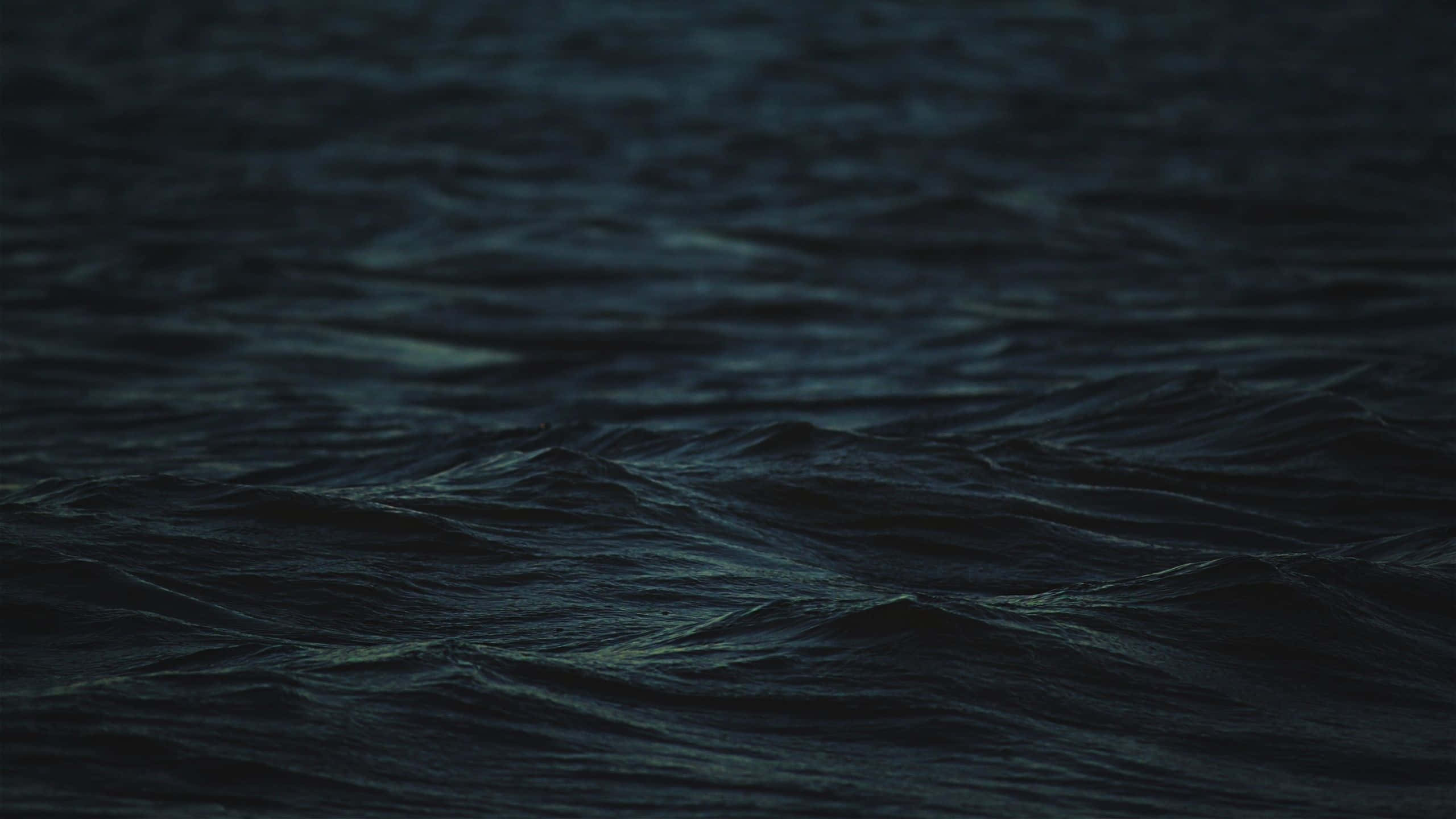 暮色中的神秘黑暗海洋 壁紙 — 深色海浪在昏暗光线下泛起漣漪，深藍與黑色調營造出憂鬱的夜間海景。