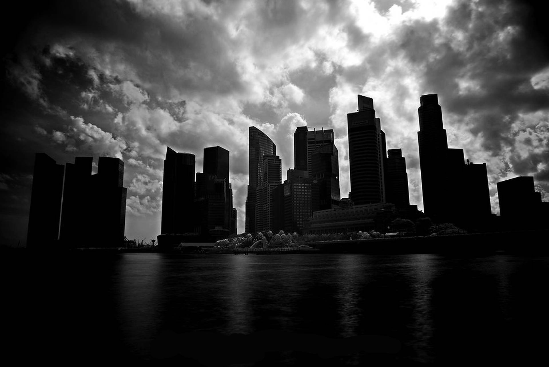 城市天際線剪影，摩天大樓在暴風雨的天空下倒映在水中。 — 暗夜城市 壁紙