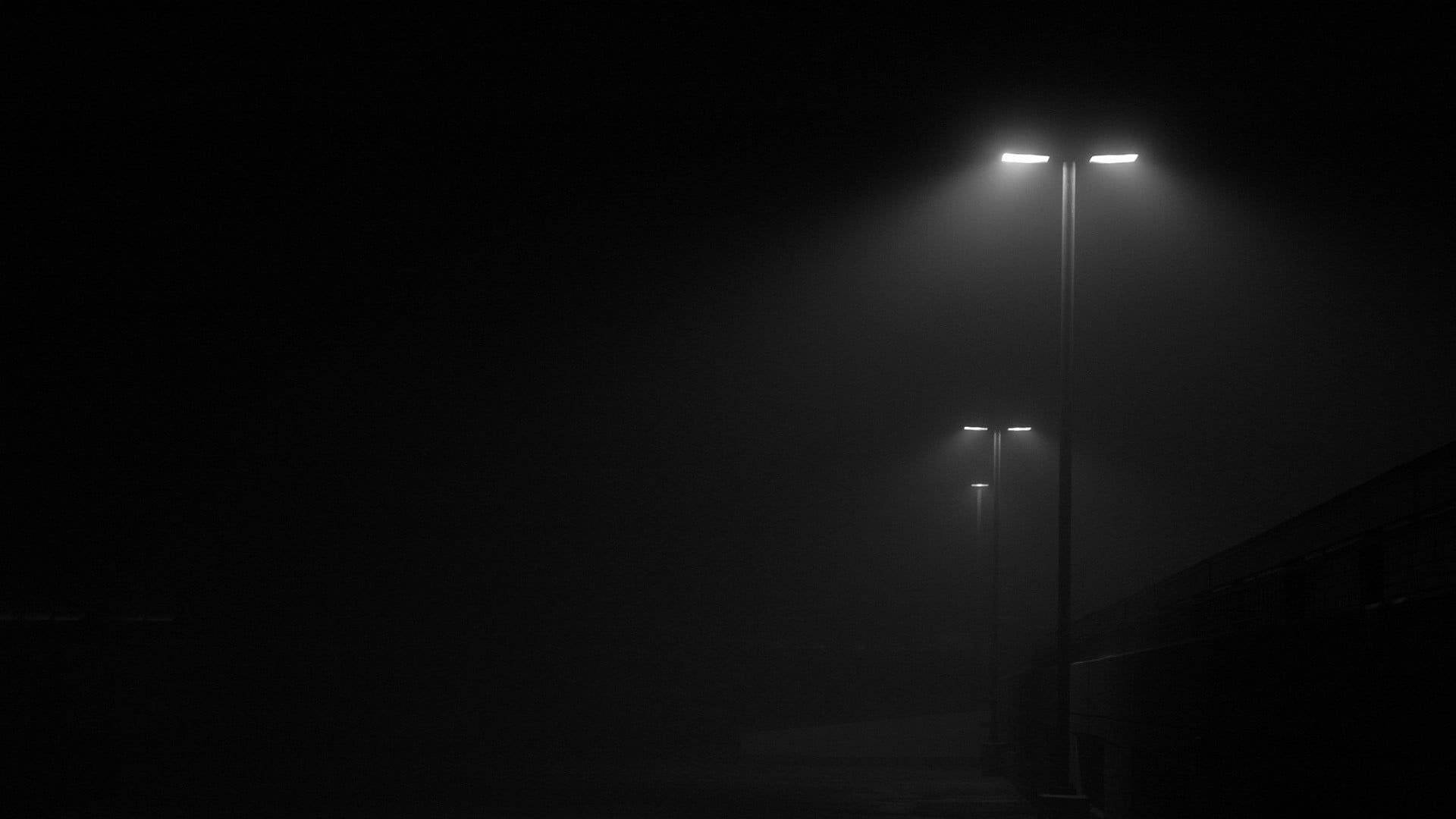 霧氣瀰漫的城市街道在夜晚被高聳的路燈照亮，光束穿過霧氣。