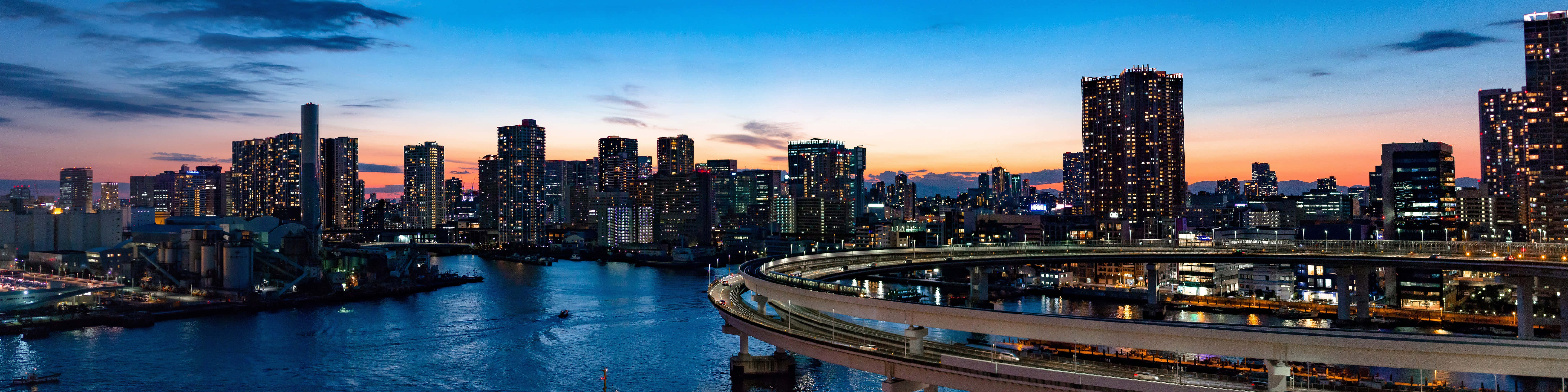 暮色城市風光超高清雙螢幕壁紙 壁紙 — 東京天際線的黃昏全景，發光的摩天大樓和彎曲的高速公路倒映在河中。