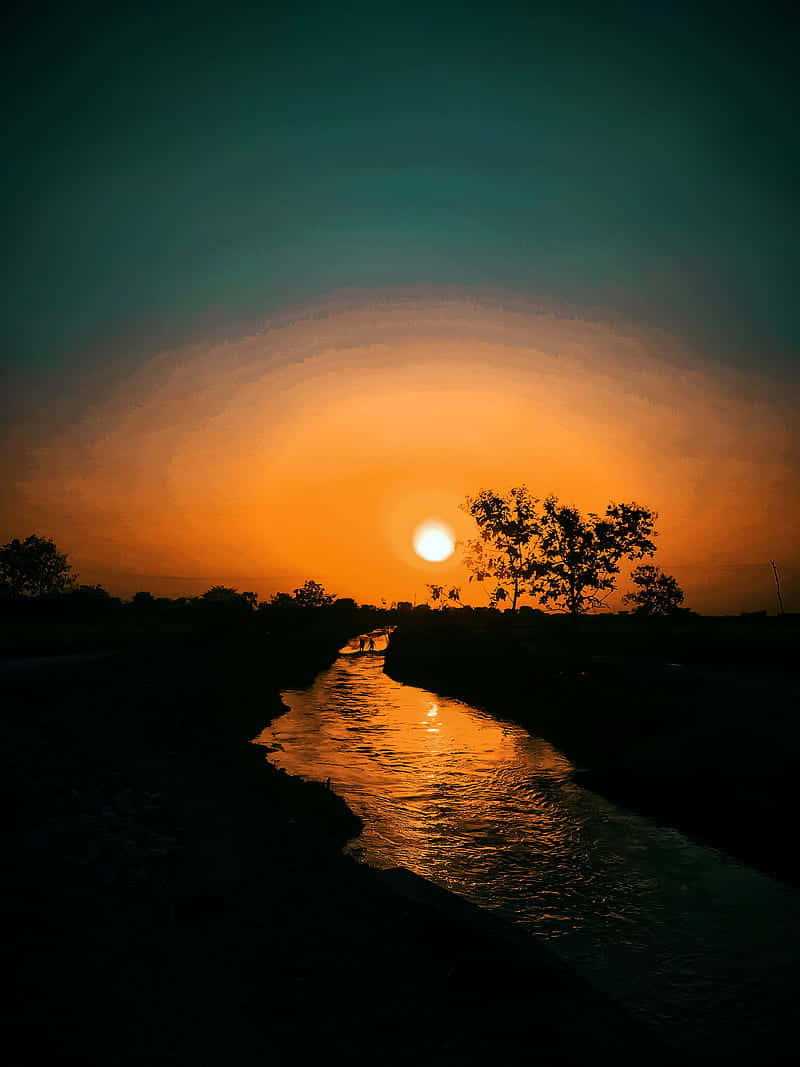 暮色天空下的河流 壁紙 — 寧靜的日落將金色光芒灑在一條蜿蜒的河流上，有剪影般的樹木和地平線上閃耀的太陽。
