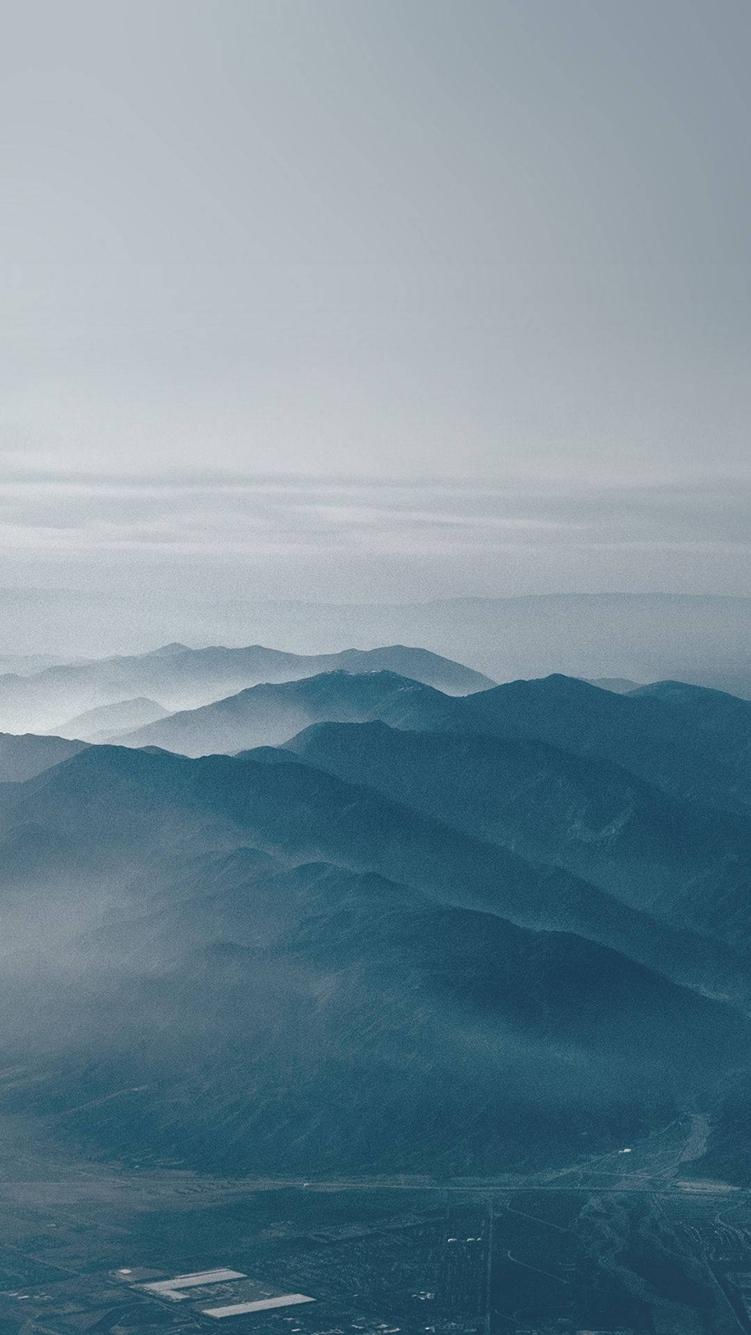 暮色天際 壁紙 — 層層疊疊的山脈在蒼白的天空下逐漸消失在霧氣中，下方是遙遠的山谷。