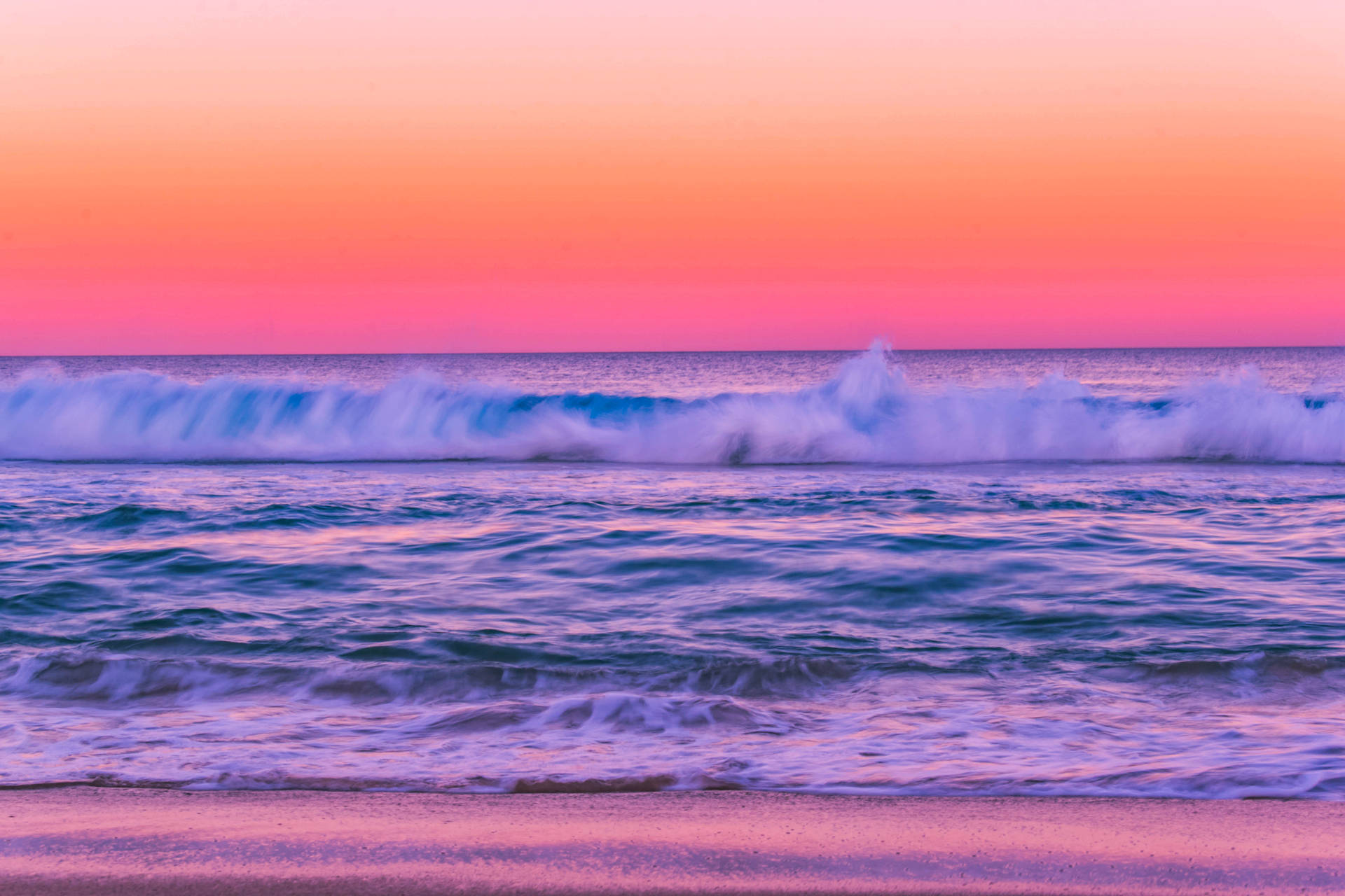 粉紅和紫色的夕陽映照在拍打沙灘的海浪上。