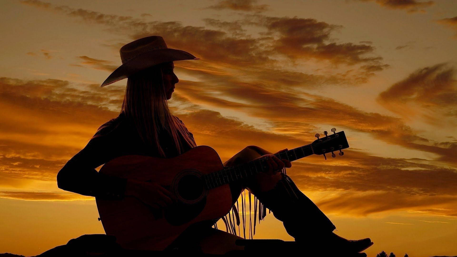戴牛仔帽女子在日落時彈結他