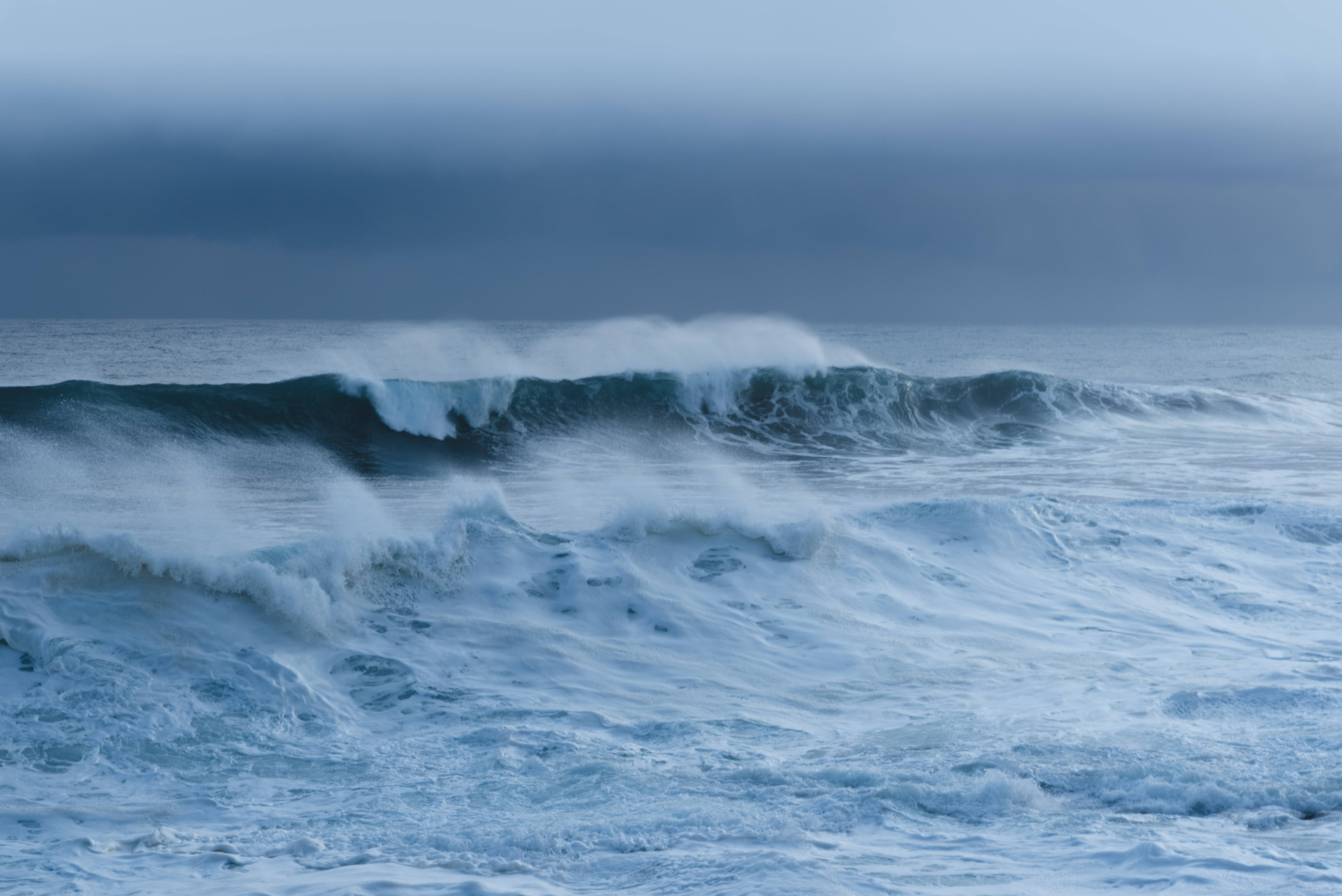 暴風雨中的海浪 壁紙 — 強勁的海浪在沉重的暴風雨天空下破碎，形成戲劇性的單色藍色場景。