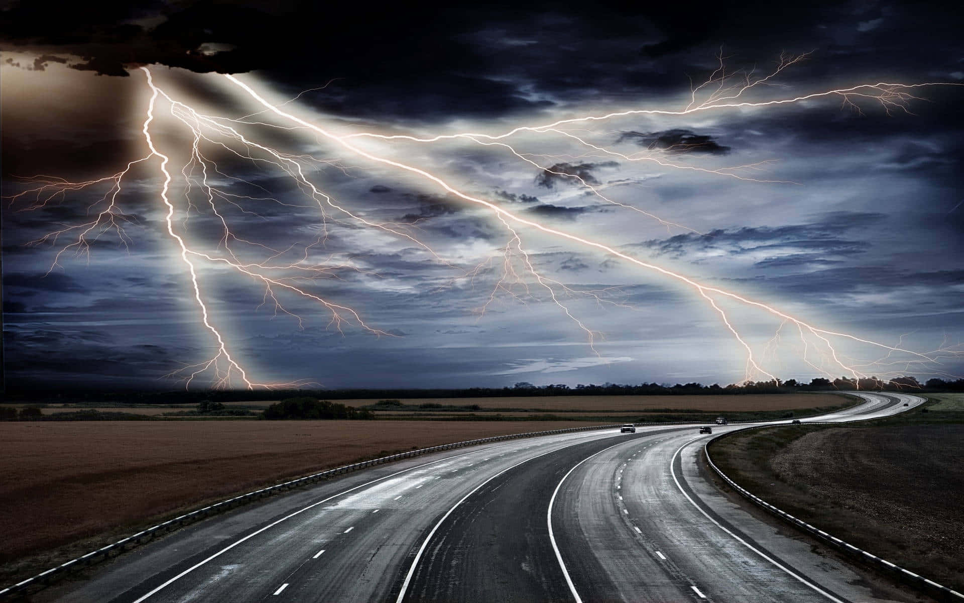 暴風雨傍晚的寧靜天空 壁紙 — 一條戲劇性的高速公路在暴風雨的天空下蜿蜒，多道閃電照亮了烏雲和濕漉漉的瀝青路面。
