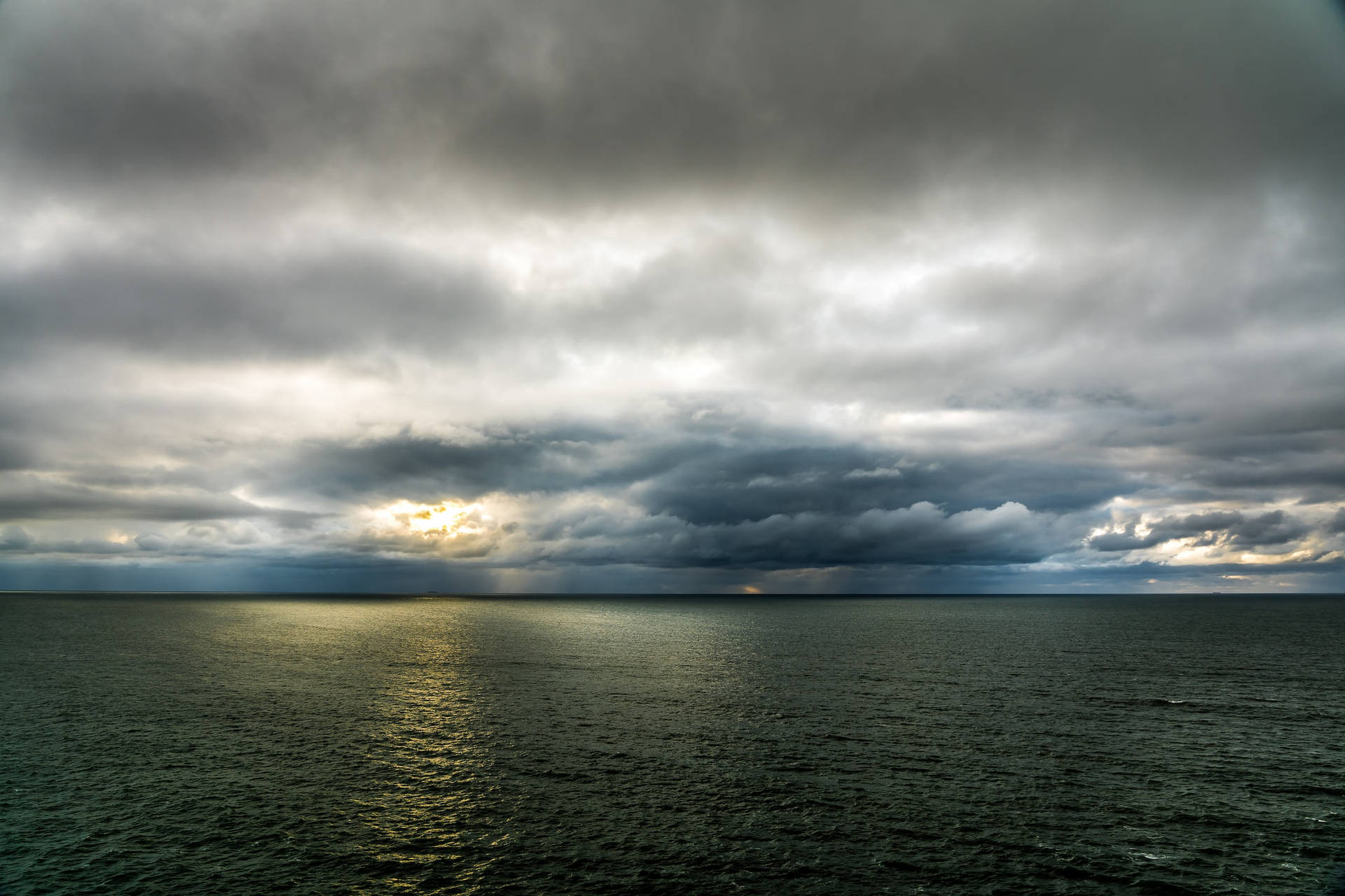 暴風雨中的海洋，陽光從地平線上的烏雲中穿透而出。