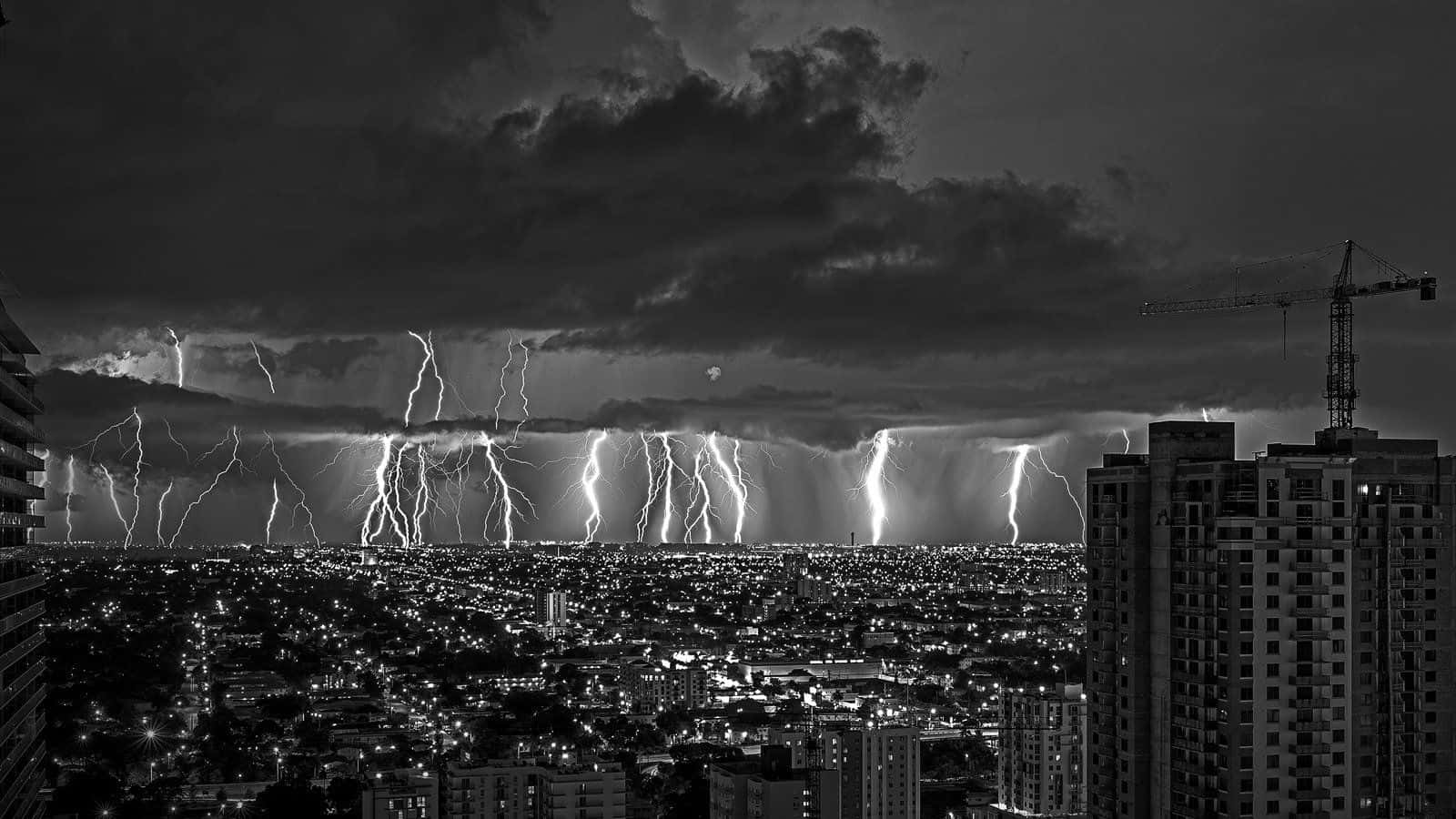 「暴風雨即將過去」 壁紙 — 一個戲劇性的黑白城市夜景，被巨大的雷暴照亮城市天際線。