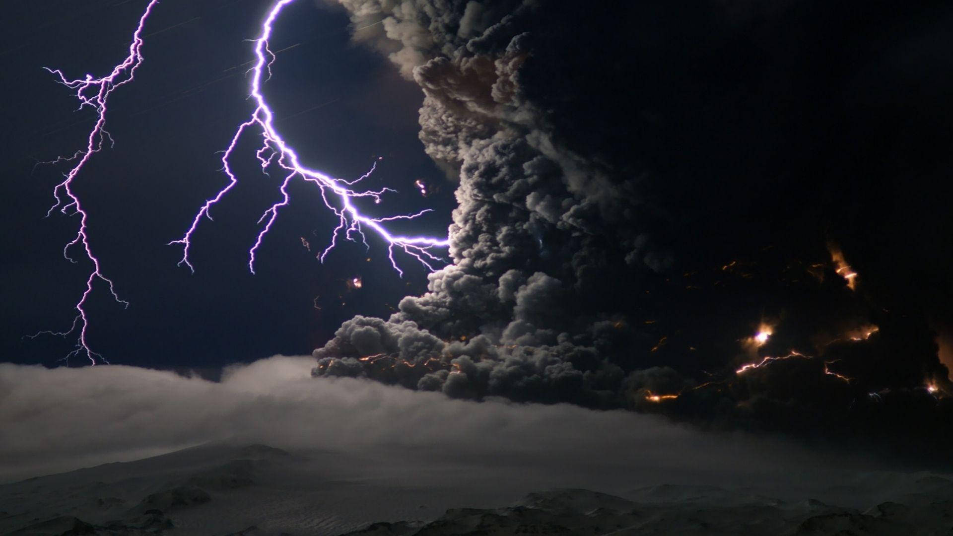 暴風雲產生電力 壁紙 — 夜間火山爆發，巨大火山灰柱和熾熱熔岩流周圍有鮮紫色閃電劃過。