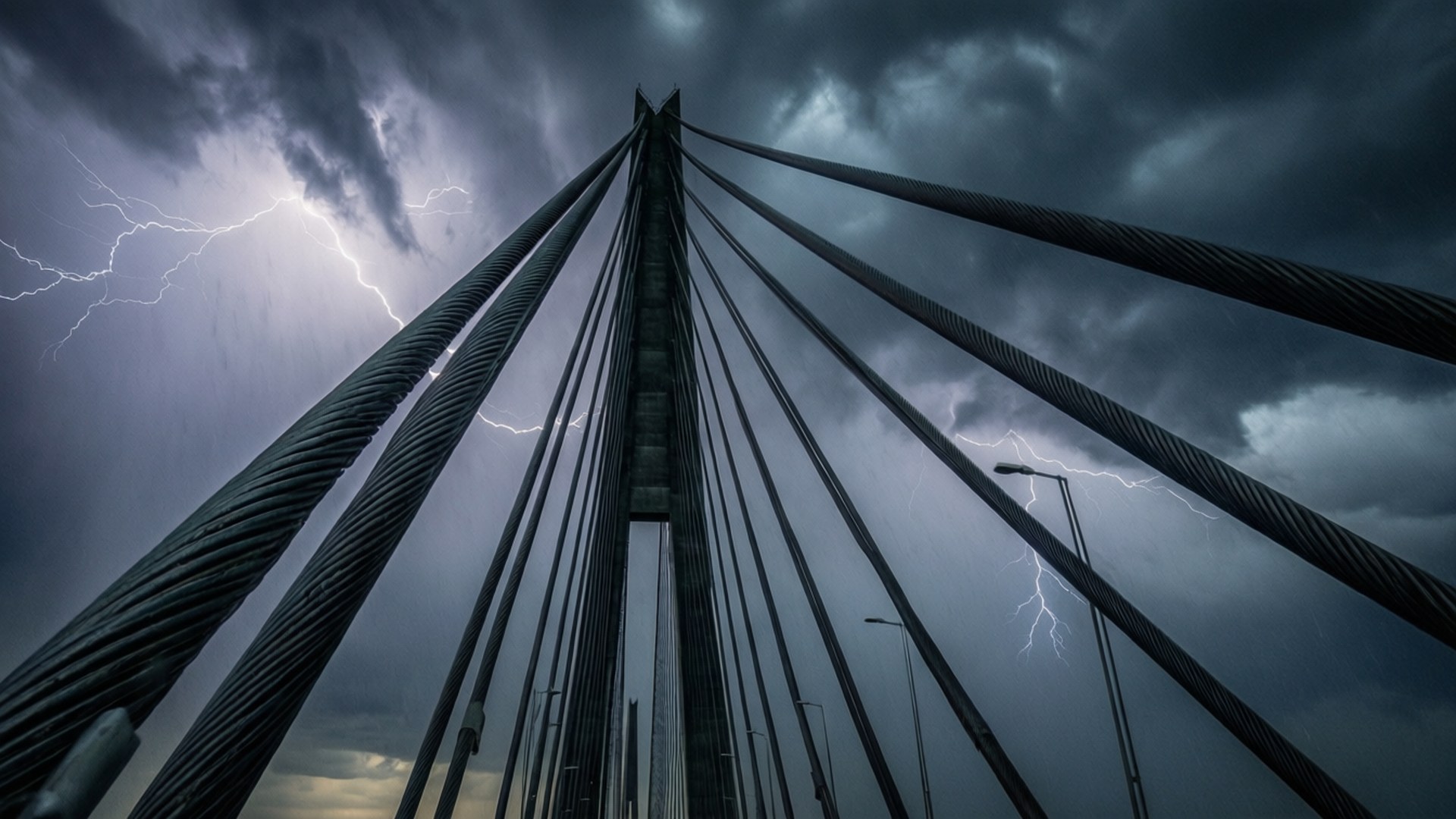 暴風雲繫索細節 壁紙 — 以低角度拍攝懸索橋纜索，背景是風雨交加的天空，伴隨 vivid 閃電的戲劇性畫面。