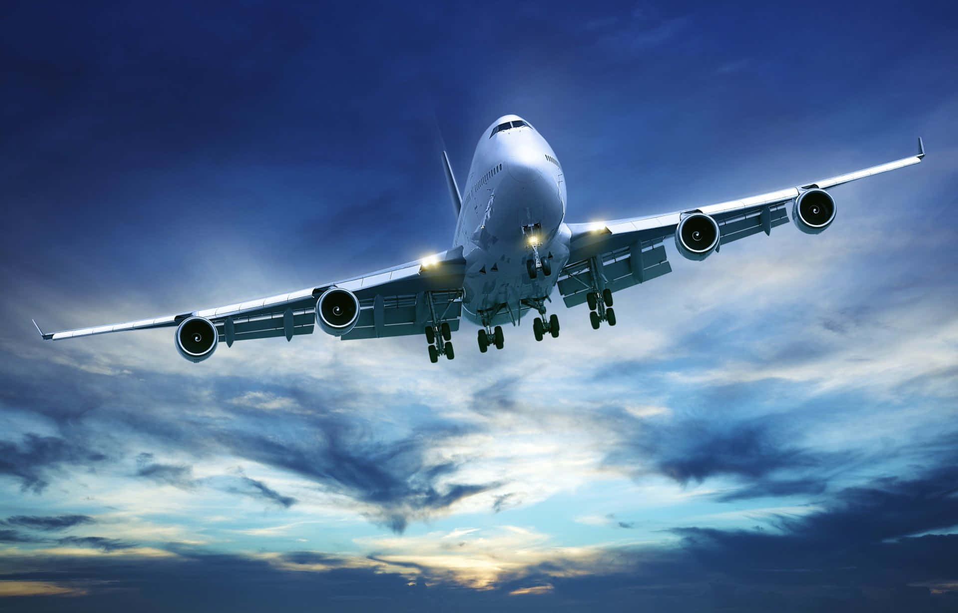 暴風雲與飛機背景 壁紙 — 一架巨大的白色珍寶客機正在下降，起落架放下，背景是帶有藍色和金色雲彩的戲劇性暮色天空。
