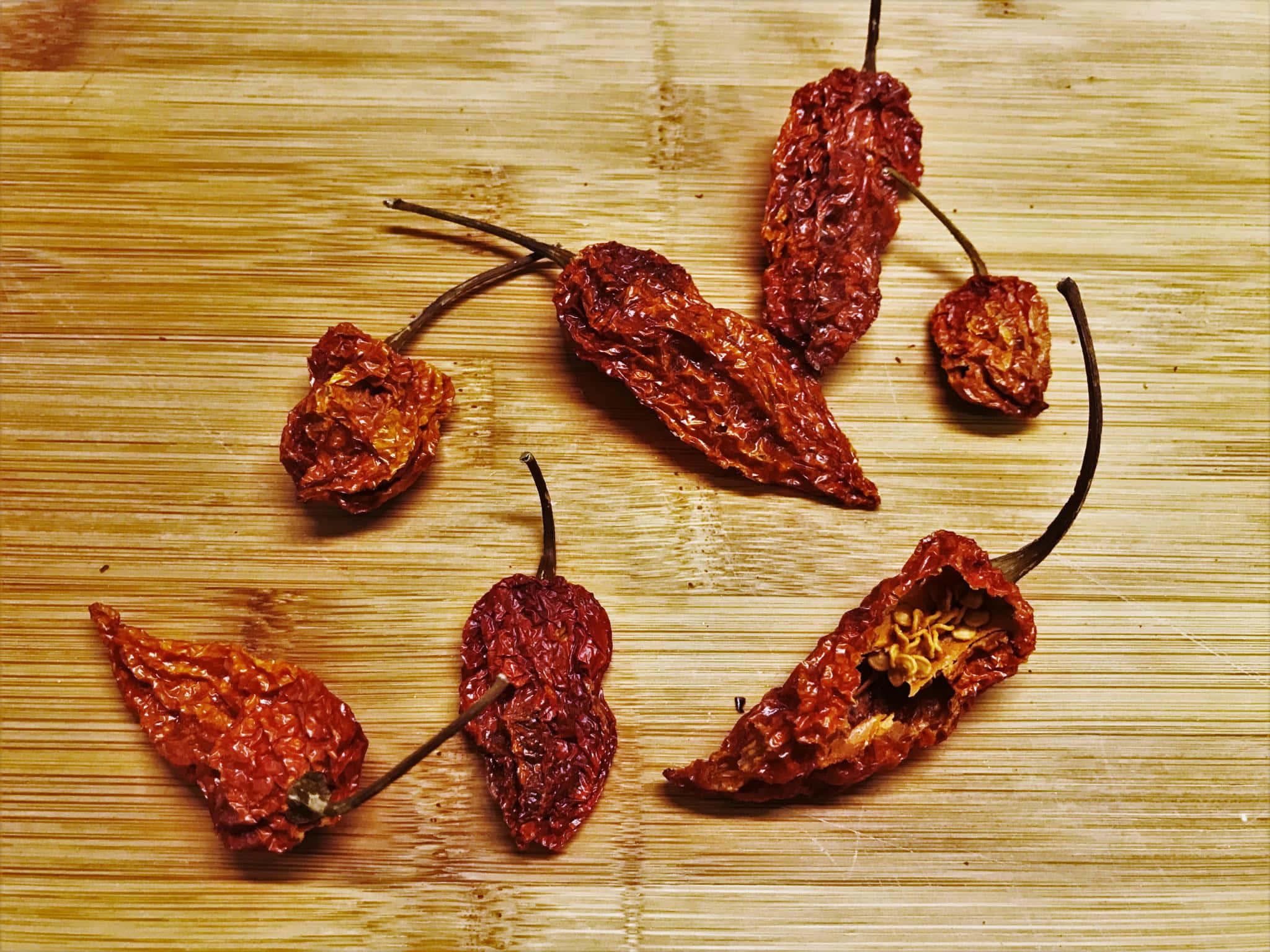 Ghost Pepper 桌布 壁紙 — 曬乾的紅辣椒，表皮皺縮，籽粒可見，放在淺色木砧板上。