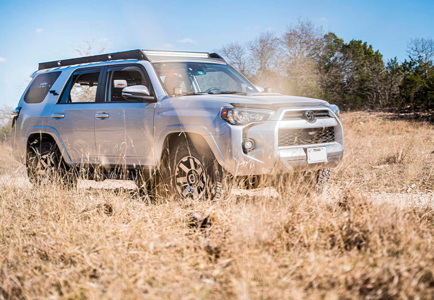 更新且具備能力——2023款Toyota 4Runner 壁紙 — 一輛銀色豐田4Runner SUV在晴朗的藍天下駛過高高的乾草，揚起灰塵。
