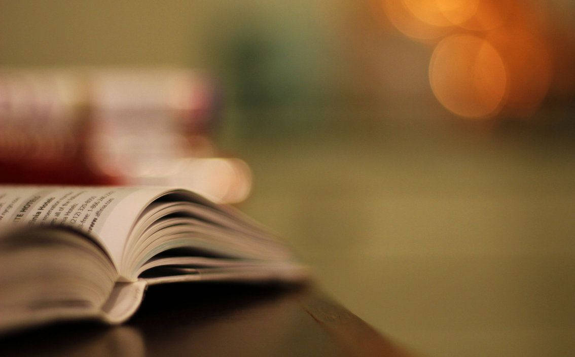 木桌上的打開的書，後面有溫暖模糊的燈光。