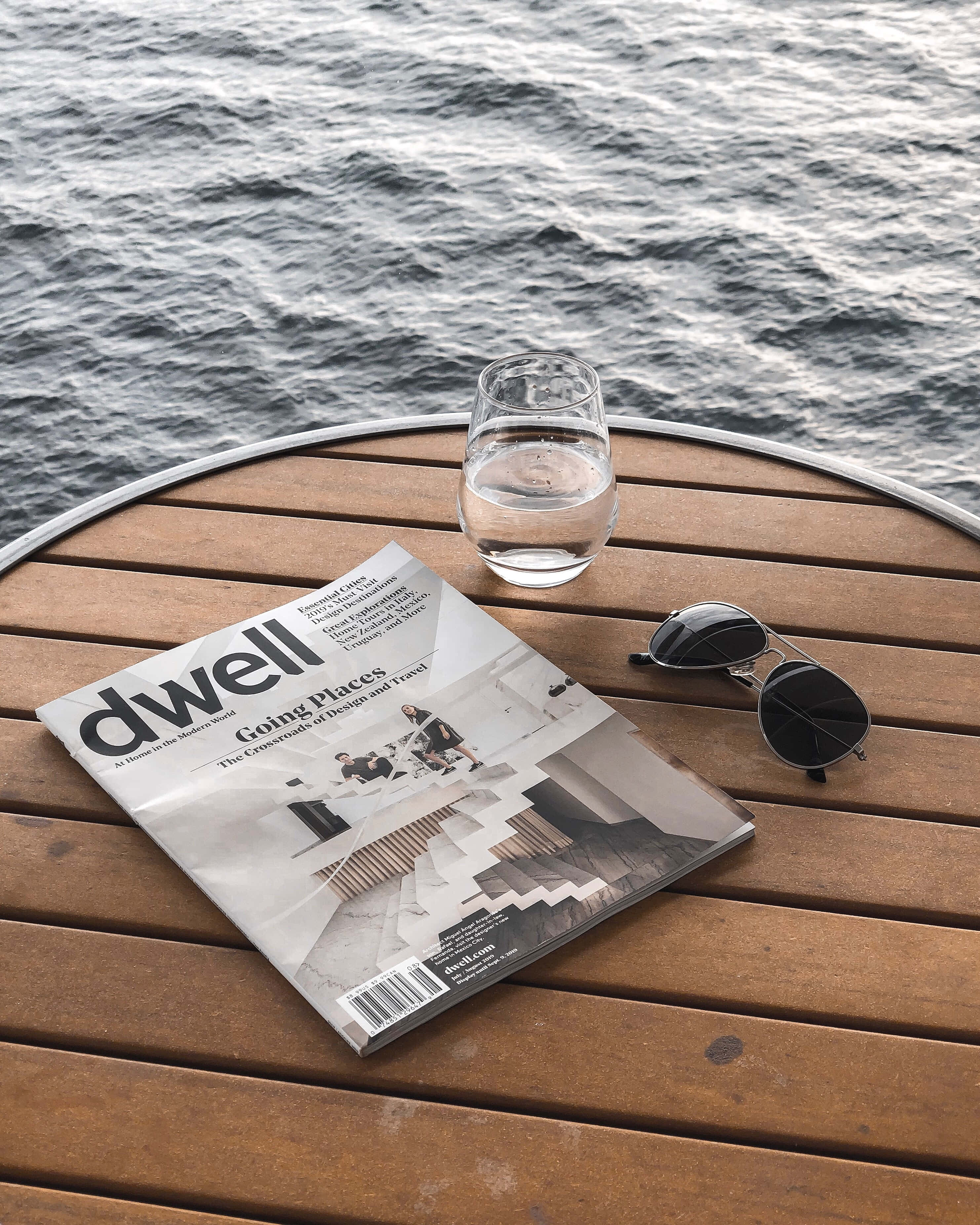 書架上各色雜誌封面 壁紙 — 雜誌杯和太陽眼鏡放在木甲板上，俯瞰漣漪的水面。