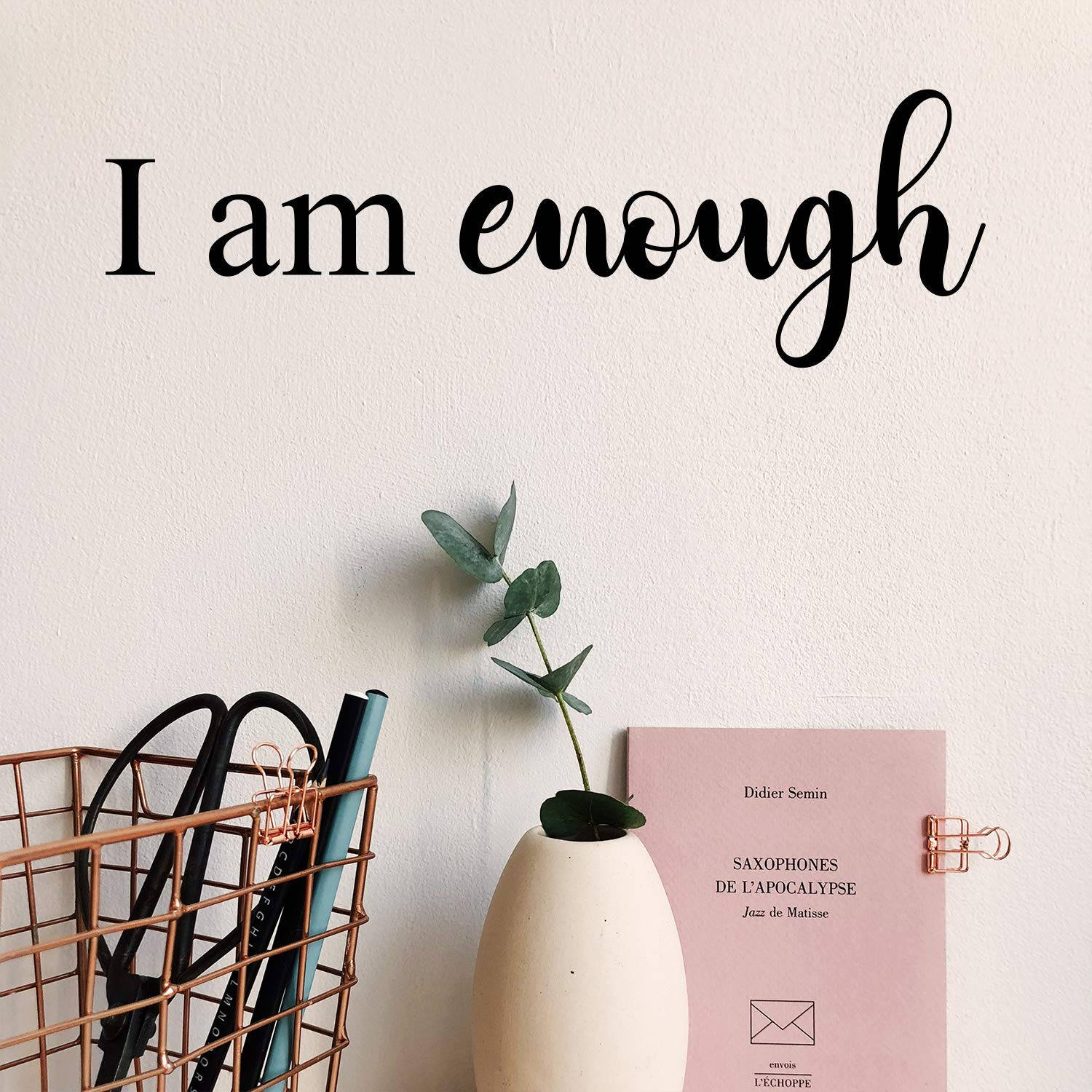 牆上有「I am enough」文字、尤加利葉花瓶、粉紅色書本和銅籃。