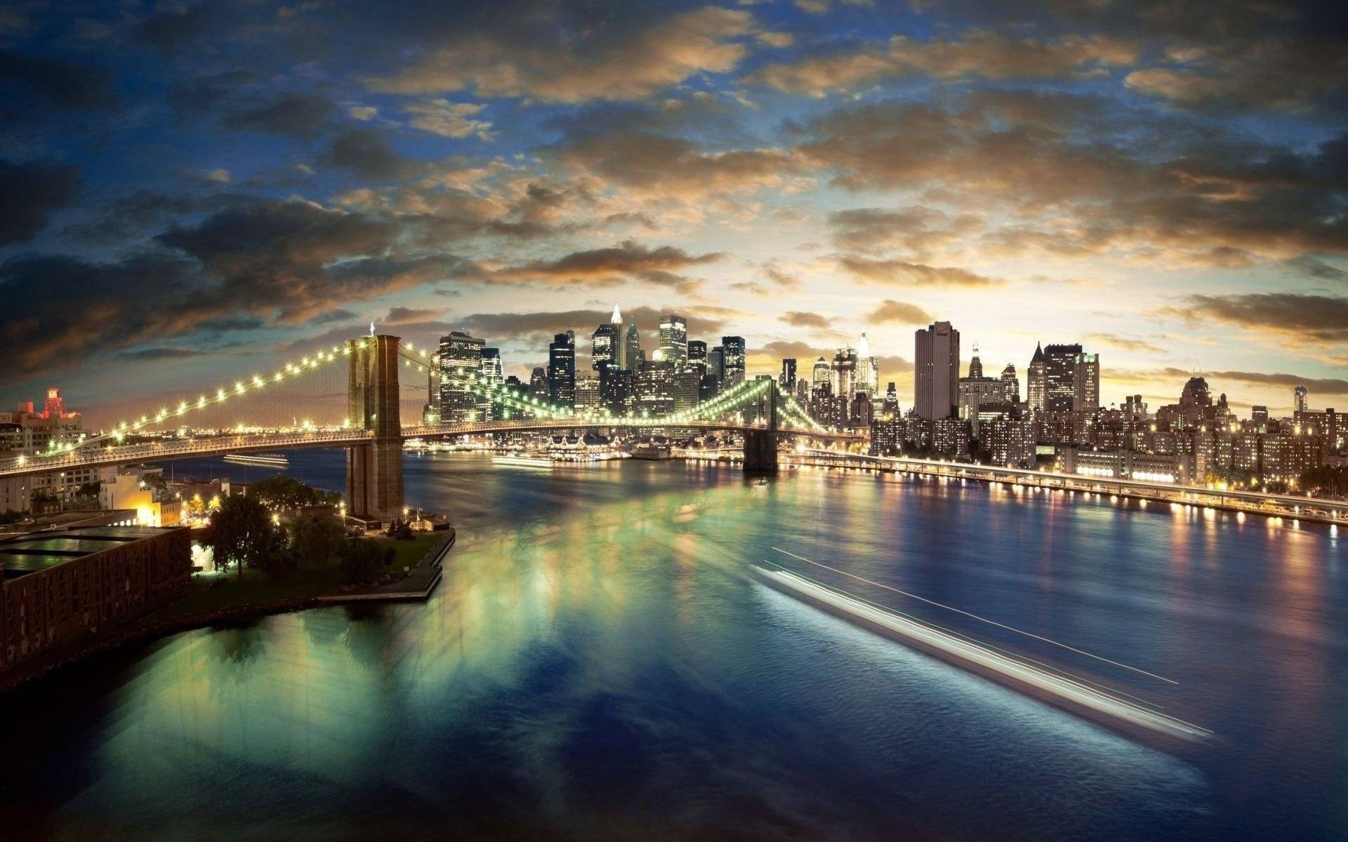 暮色中亮燈的布魯克林大橋，城市天際線與河面倒影。