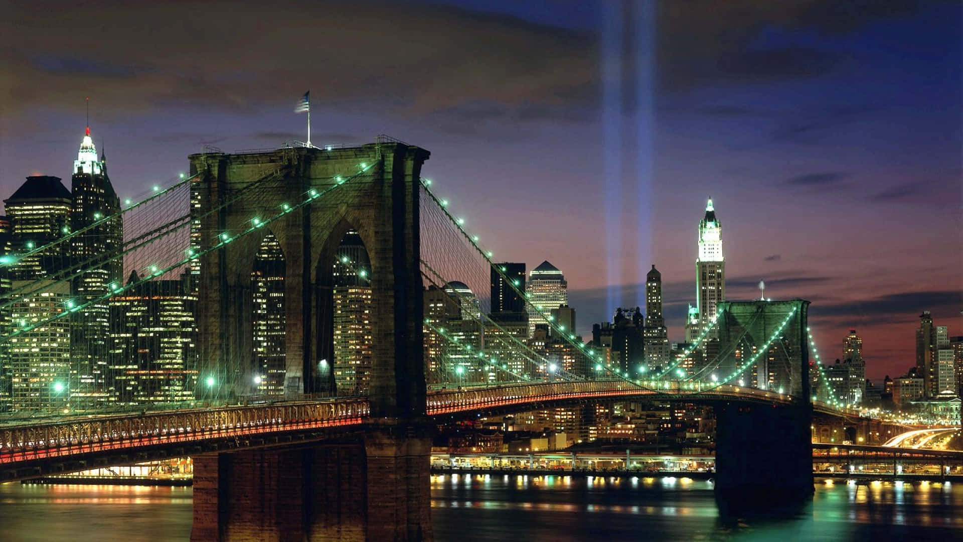 布魯克林大橋在黃昏時亮起，Tribute in Light 光束在曼哈頓天際線上升起。