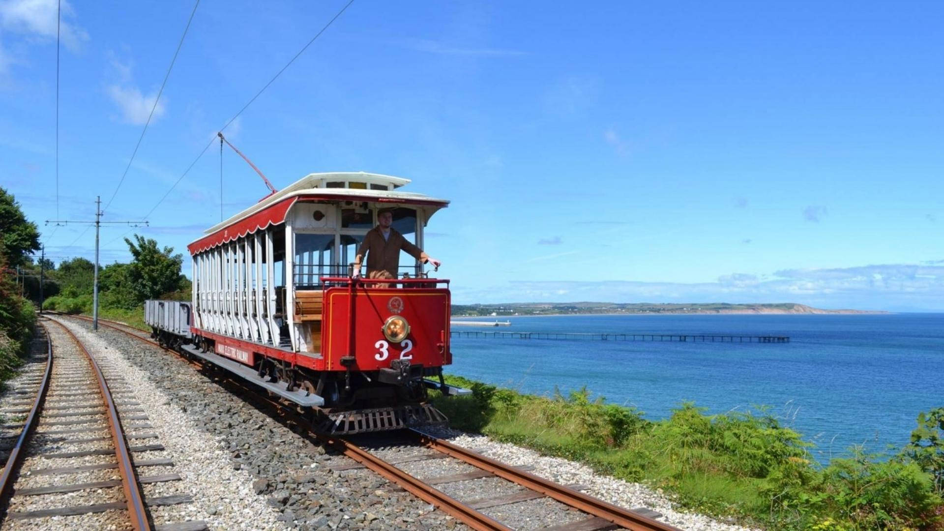 曼島曼克電氣鐵路 壁紙 — 一輛紅色復古露天火車32號沿著海岸線行駛，在晴朗的藍天下，可以看到海洋和碼頭。