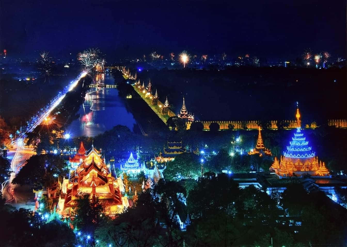夜晚發光的寺廟建築群，運河上空有煙火。