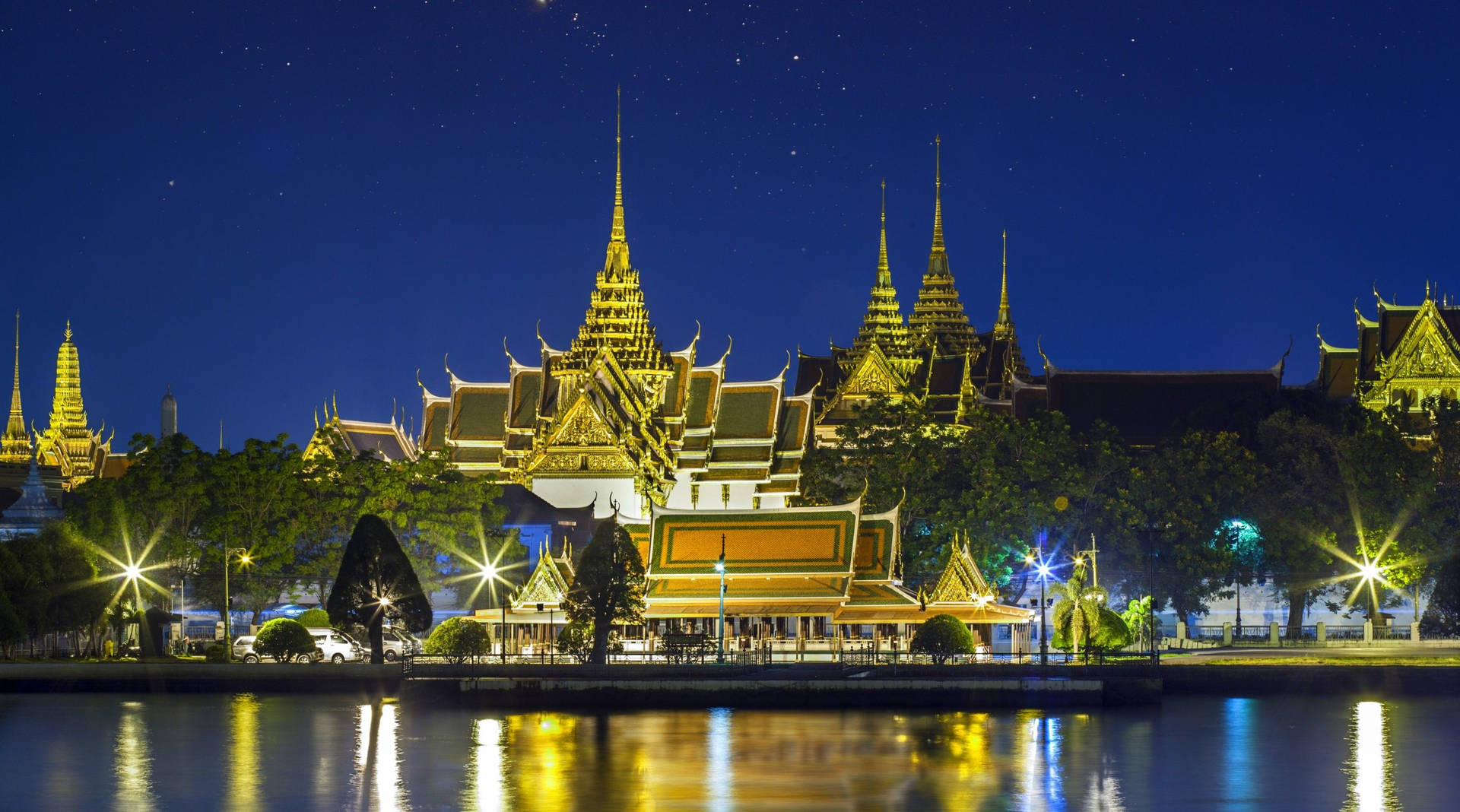 夜晚燈光下的金色寺廟建築群，星空與水面倒影。