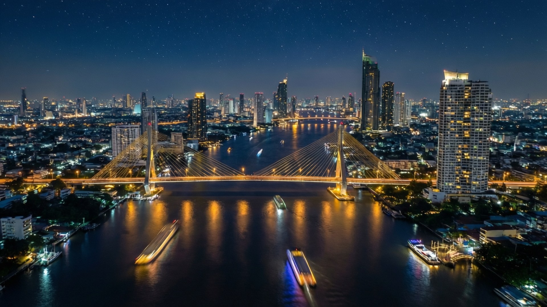 曼谷河畔夜景 壁紙 — 曼谷天際線的夜間空中景觀，一座發光的斜拉橋橫跨滿載移動船隻的河流，星空下。