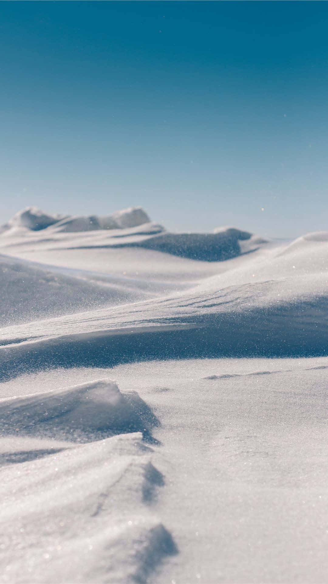 冬季晴朗藍天下，白雪覆蓋的沙丘和山脈。