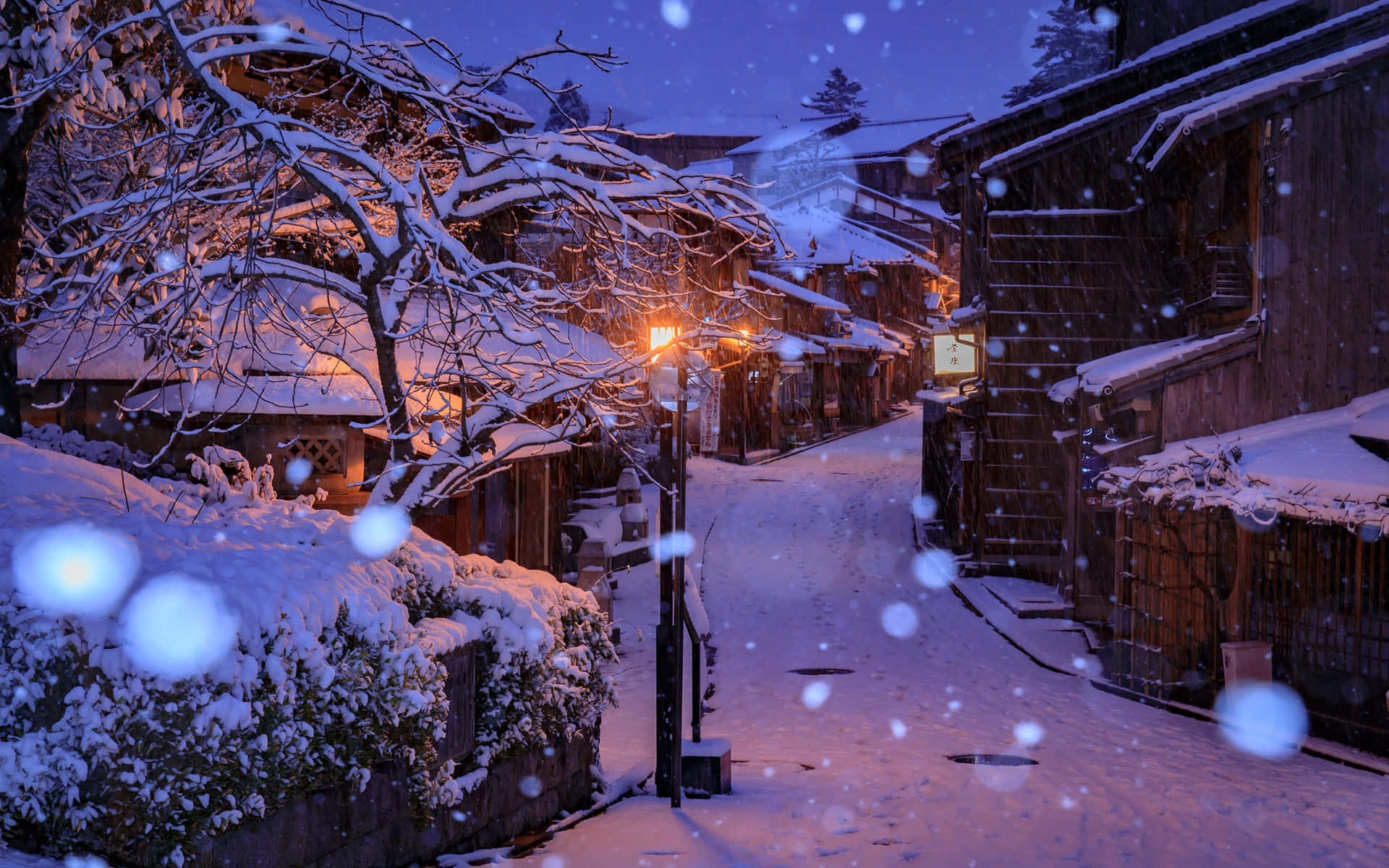夜晚積雪的村莊街道，燈籠閃爍，雪花飄落。