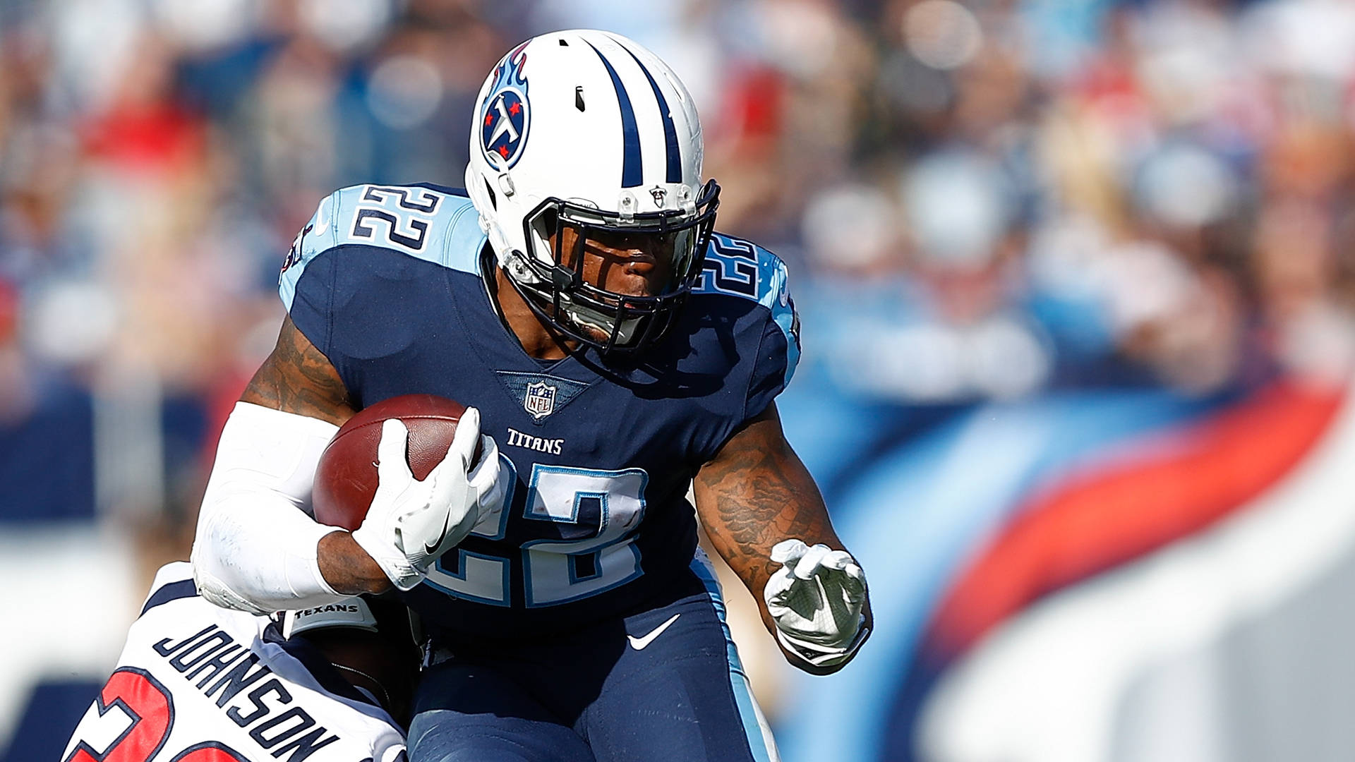 最佳接球手德里克·亨利 壁紙 — 一名身穿藍色球衣的田納西泰坦隊美式足球員，在被德州人隊球員擒抱時持球衝刺。