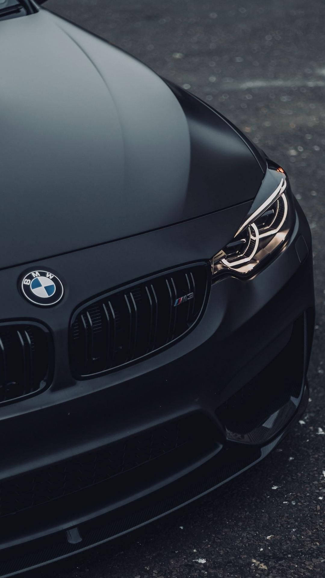 最佳暗色 BMW 車 壁紙 — 啞光黑色BMW M3跑車在瀝青路上亮起車頭燈的特寫。