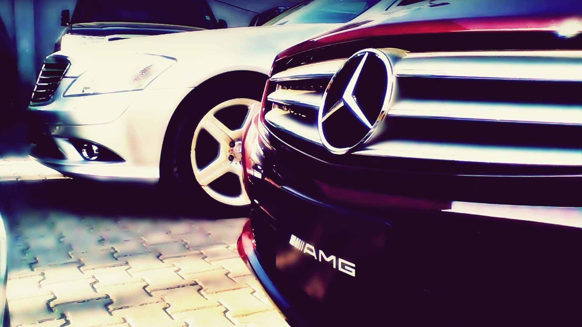 最佳梅賽德斯背景：梅賽德斯AMG Ultra前保險桿 壁紙 — 特寫一輛亮紅色 Mercedes-AMG 和白色轎車停放在圖案路面上的明亮光線下。