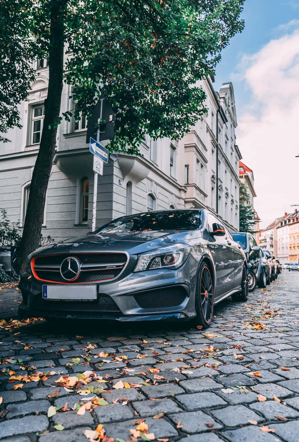 最佳梅賽德斯背景：灰色梅賽德斯-奔馳CLA 壁紙 — 一架時尚的銀色 Mercedes-AMG CLA45 停泊在鋪滿秋葉的鵝卵石街道上，天空部分多雲。