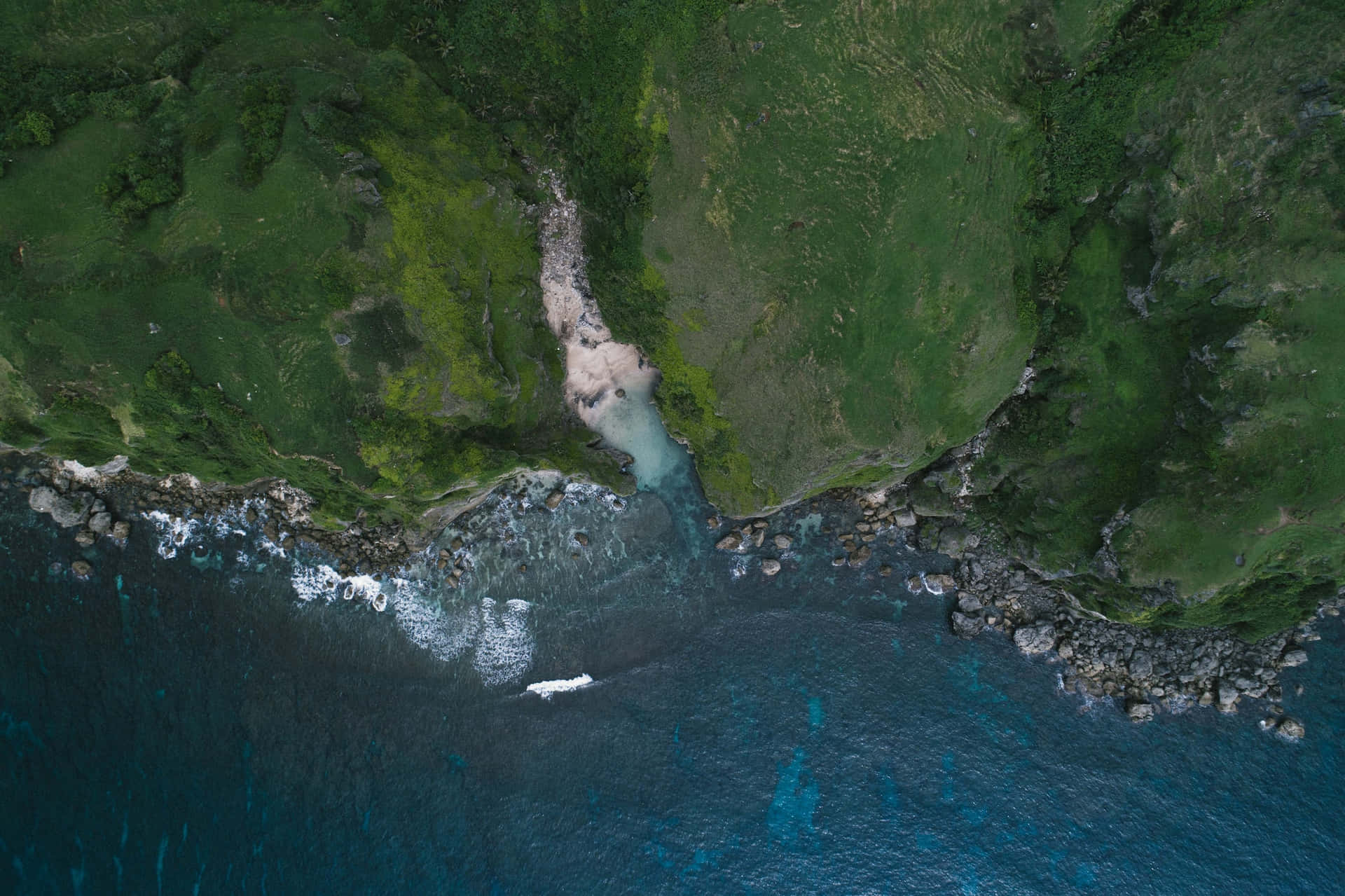 從高空俯瞰，一個隱藏的海灣，擁有藍綠色的海水，被綠色懸崖和拍岸的海浪環繞。