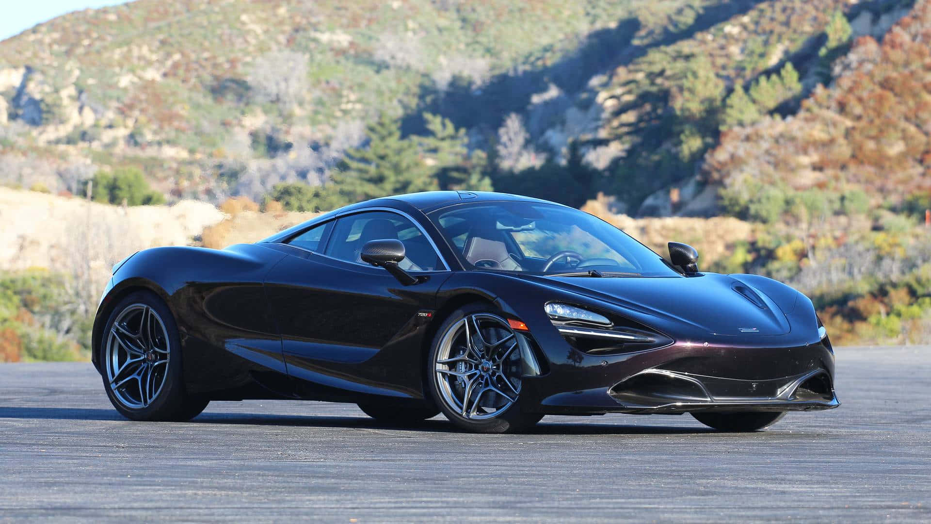 黑色McLaren 720S跑車停泊在道路上，背景是秋日山景。