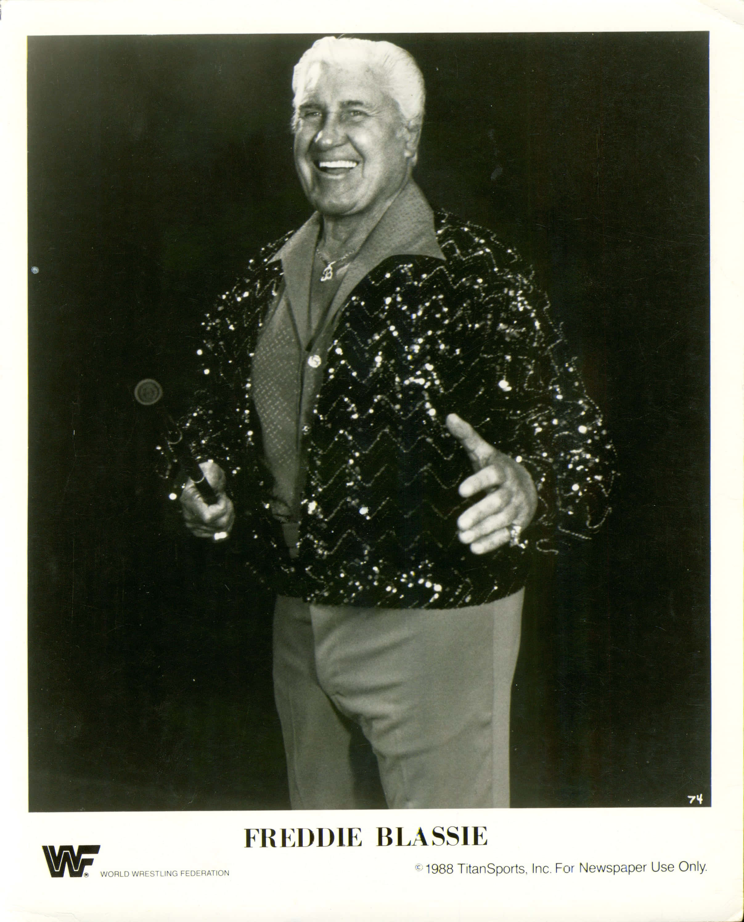 最偉大的職業摔角手弗雷迪·布拉斯比 壁紙 — Freddie Blassie 身穿閃亮亮片外套，手持麥克風，在深色背景下咧嘴大笑。
