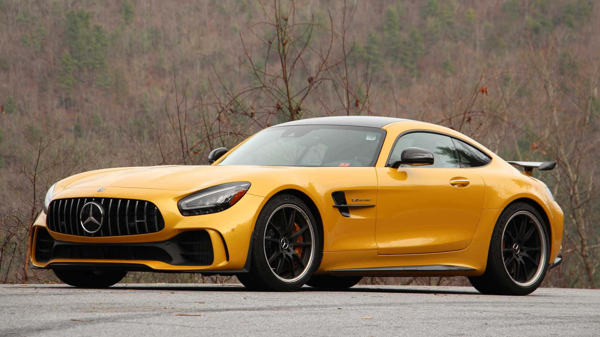 黃色 Mercedes-AMG GT R 跑車停在靠近樹林覆蓋的山丘的道路上。
